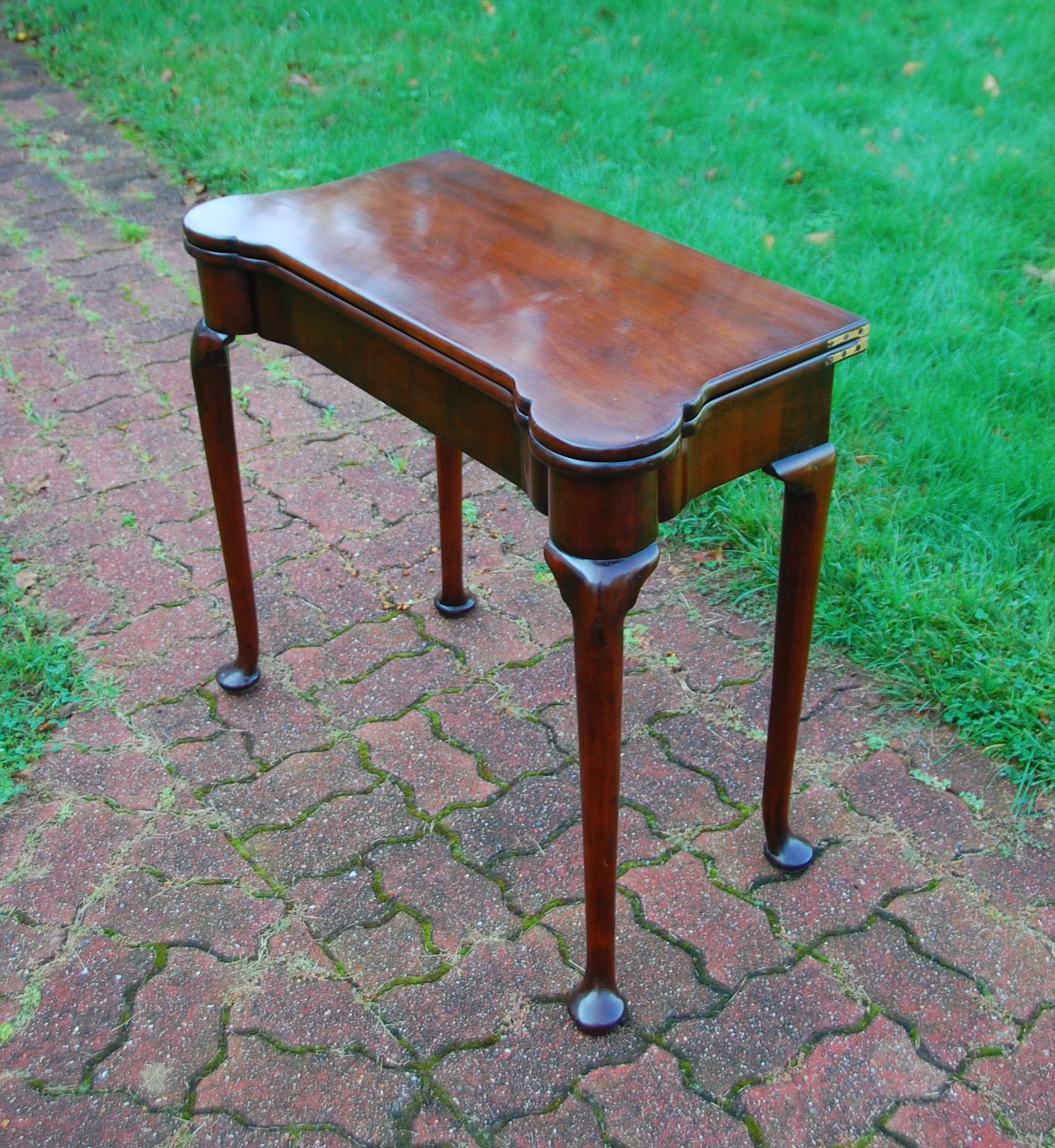 English George II mahogany foldover card table with cabriole legs, pad feet, guinea wells and candleholders. When the table is opened, the green baize playing surface is revealed. Oval guinea wells for each player, along with round corner mahogany