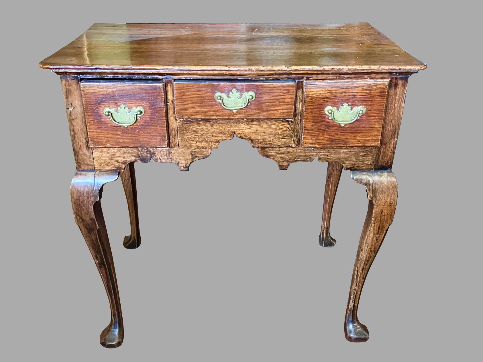 An English George II period provincial oak lowboy or dressing table of typical form, the overhanging top with a molded edge above 3 fitted drawers over a shaped apron. The piece is supported on cabriole legs ending in shaped pad feet. Appears to