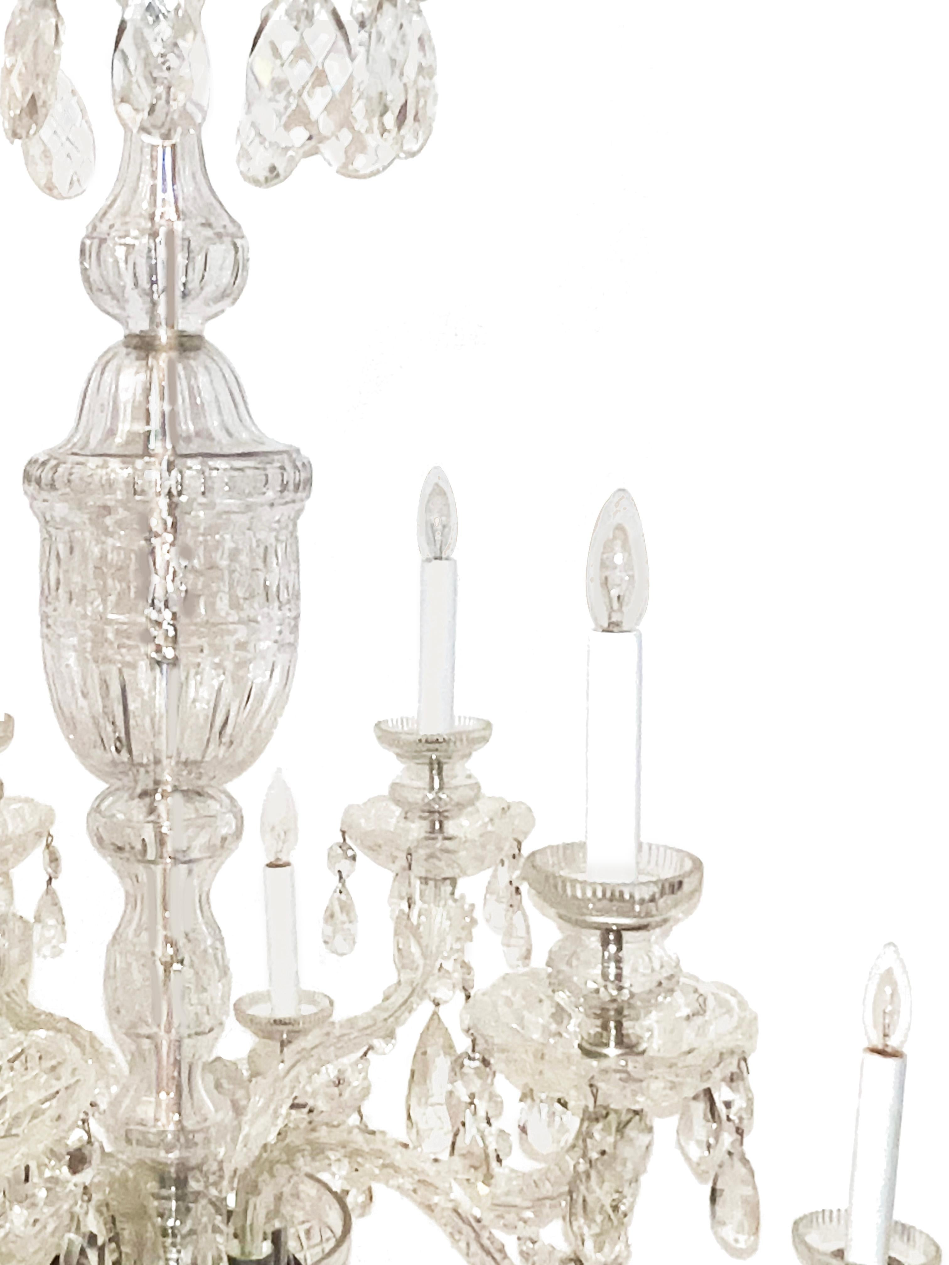An English George II style 10 light leaded glass chandelier. The center shaft with baluster and vase shaped elements covering the center rod issuing 12 arms of staggered height. The candle cups and umbrella shaped top draped with teardrop shaped