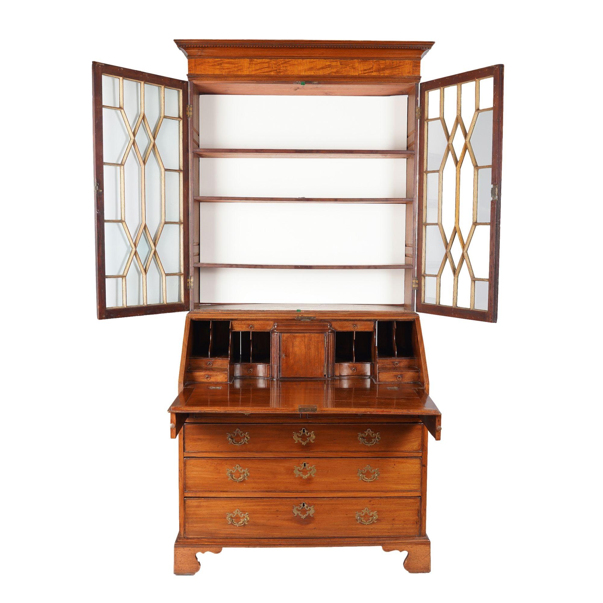 George III secretary bookcase with glazed astral doors on a slant front desk. The case is defined by a denticulated cove cut cornice above a figured mahogany entablature and astragal double doors which open to a three shelf interior. The central