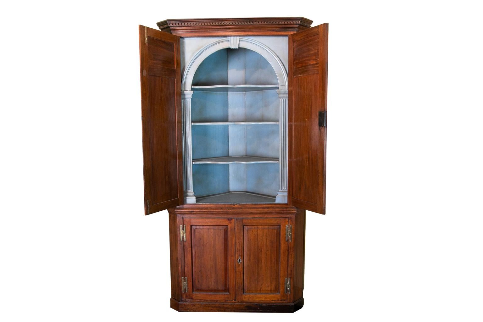 English George III corner cupboard has raised panel doors, the cornice with wall of troy molding. The interior has butterfly shelves with fluted columns and an arch with key stone. It has the original five inch brass H hinges. This piece has superb
