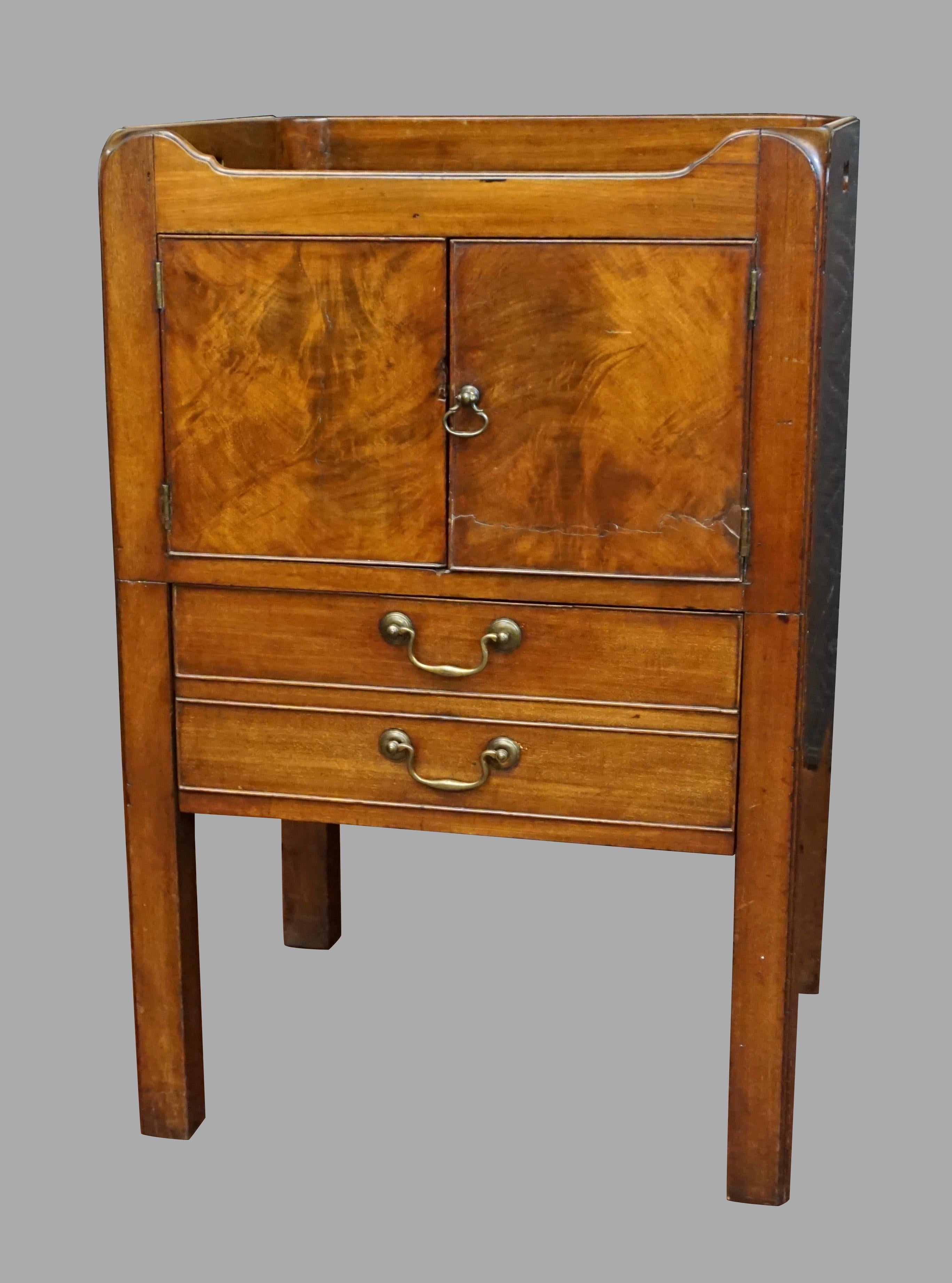 A George III figured mahogany bedside commode of typical form, the shaped top with side carrying handle cutouts, above a pair of cupboard doors over a single pull out drawer all resting on square legs. Circa 1800-1820.