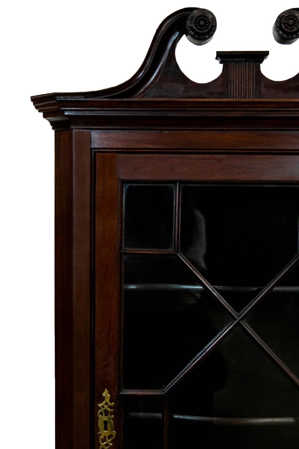 The top of this mahogany corner cupboard has the original broken arch pediment with carved floral rosettes in a fluted central plinth. The door has a classic thirteen pane window arrangement with the original wavy blown glass panes. There are three