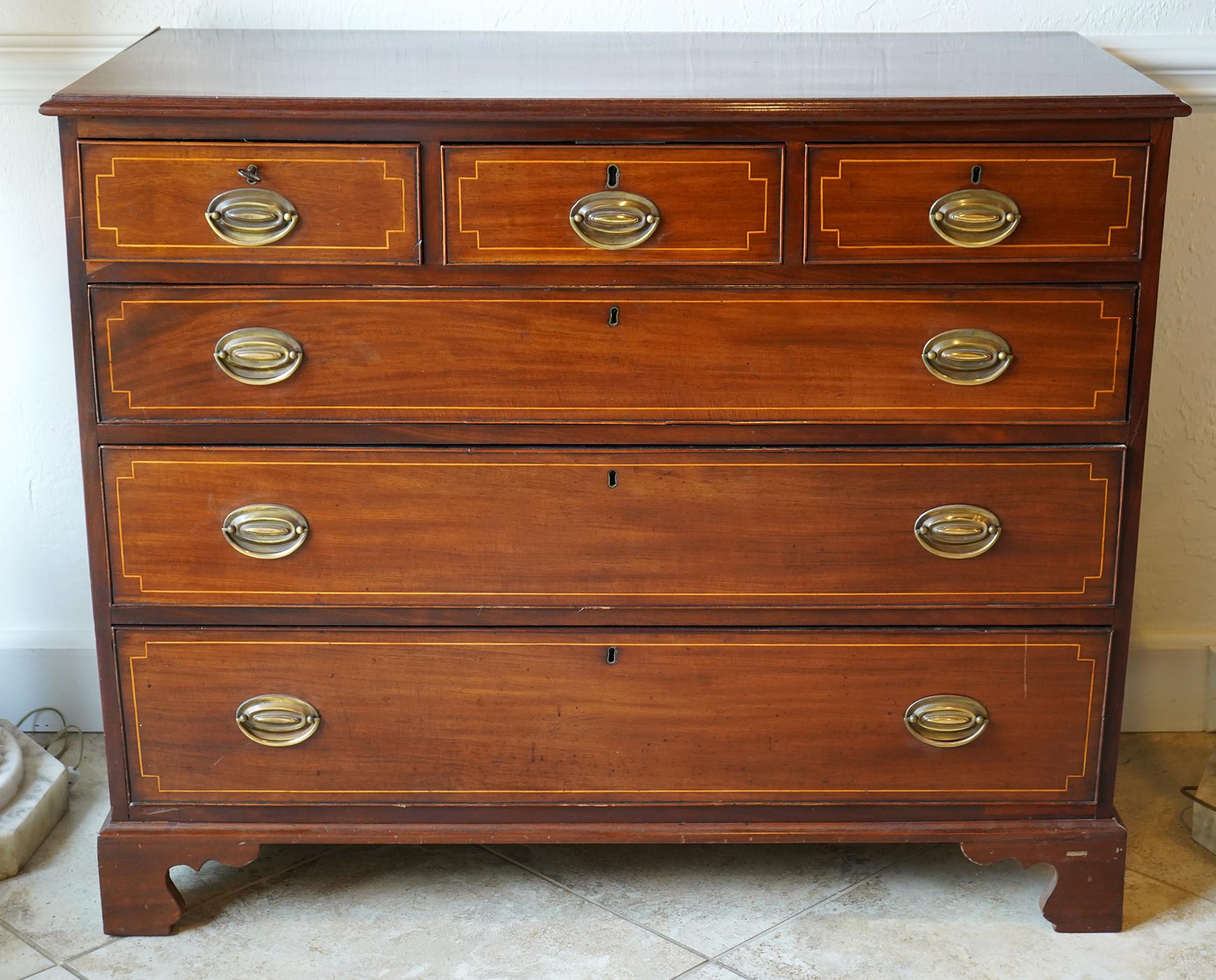 This distinguished George III mahogany chest of drawers dating to around 1820 features three short drawers above three graduated long drawers. All drawers with satinwood string inlay. The chest rests on carved bracket feet.