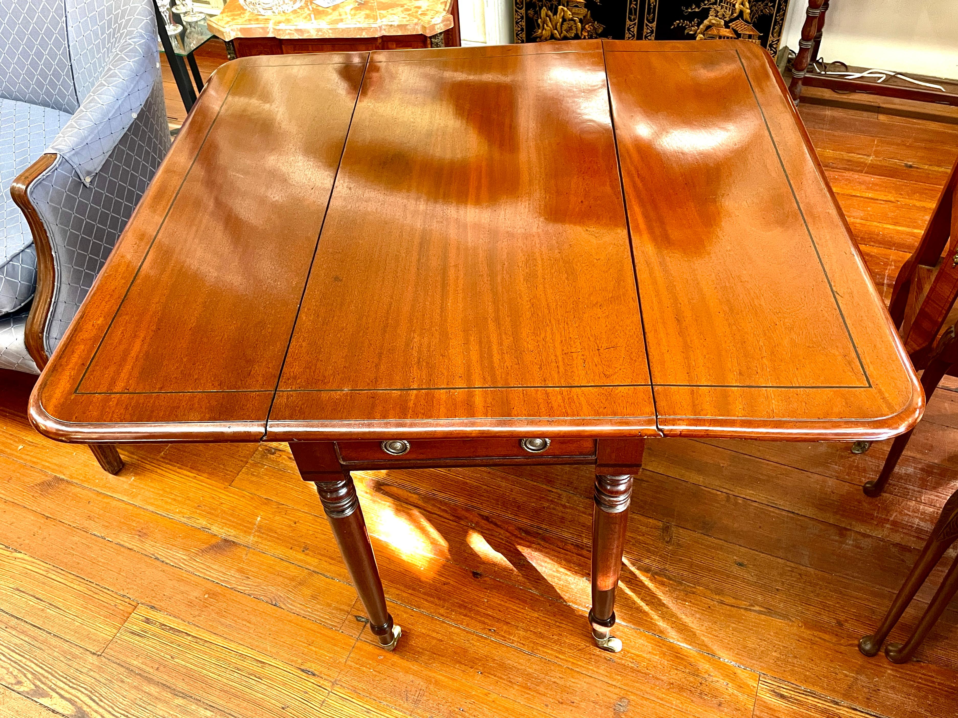 Fine and useful antique English George IV black line inlaid figured mahogany Sheraton style drop-leaf Pembroke table. 
Opens to serve as a lovely small dining table for four. Retains its original casters and finish is extraordinary and in pristine