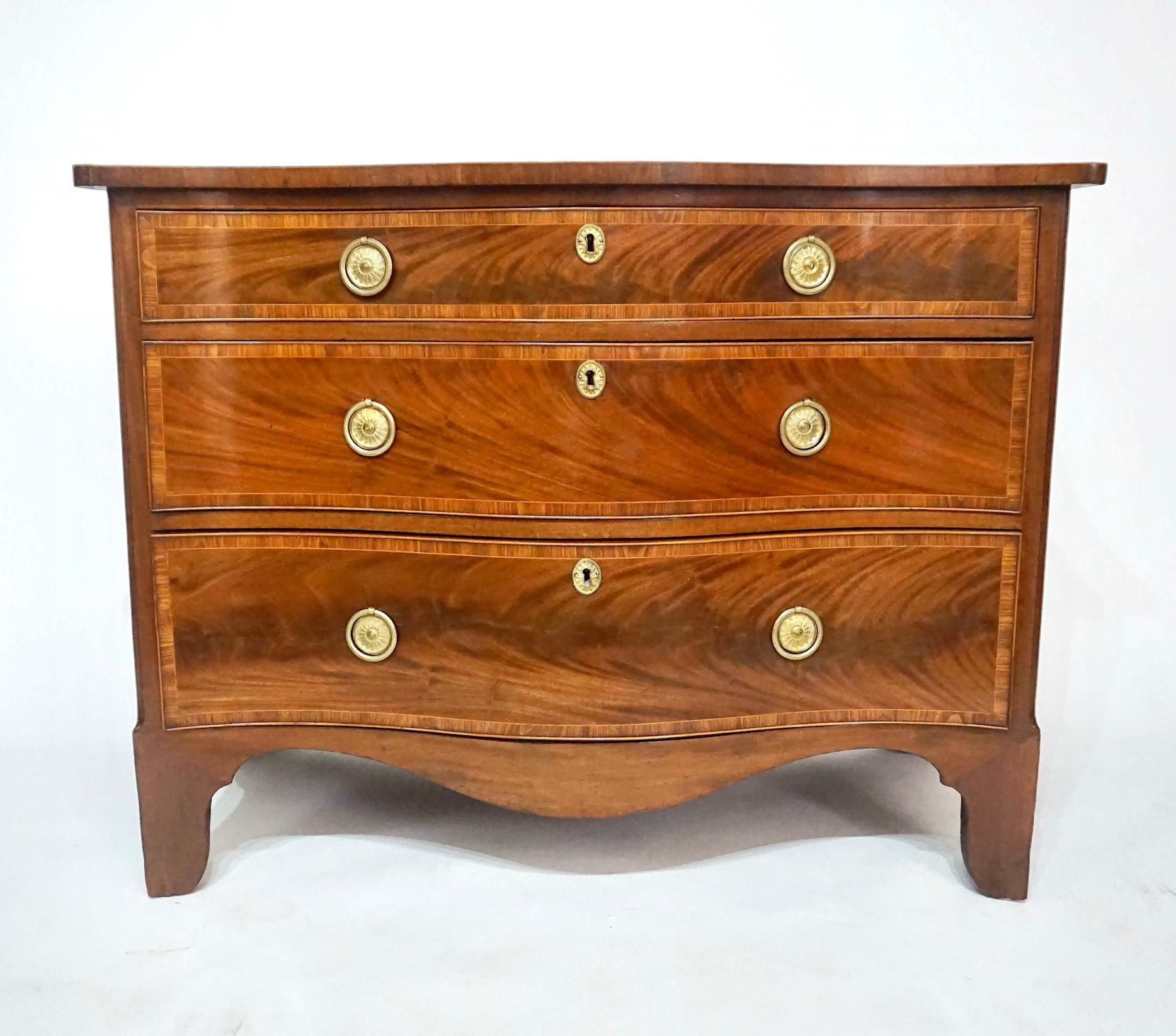 A fine circa 1785 English George III period Hepplewhite style three-drawer commode of serpentine form having exquisitely grained crotch mahogany veneers with kingwood crossbanding and  satinwood cockbeading and line-inlay, the drawers with original