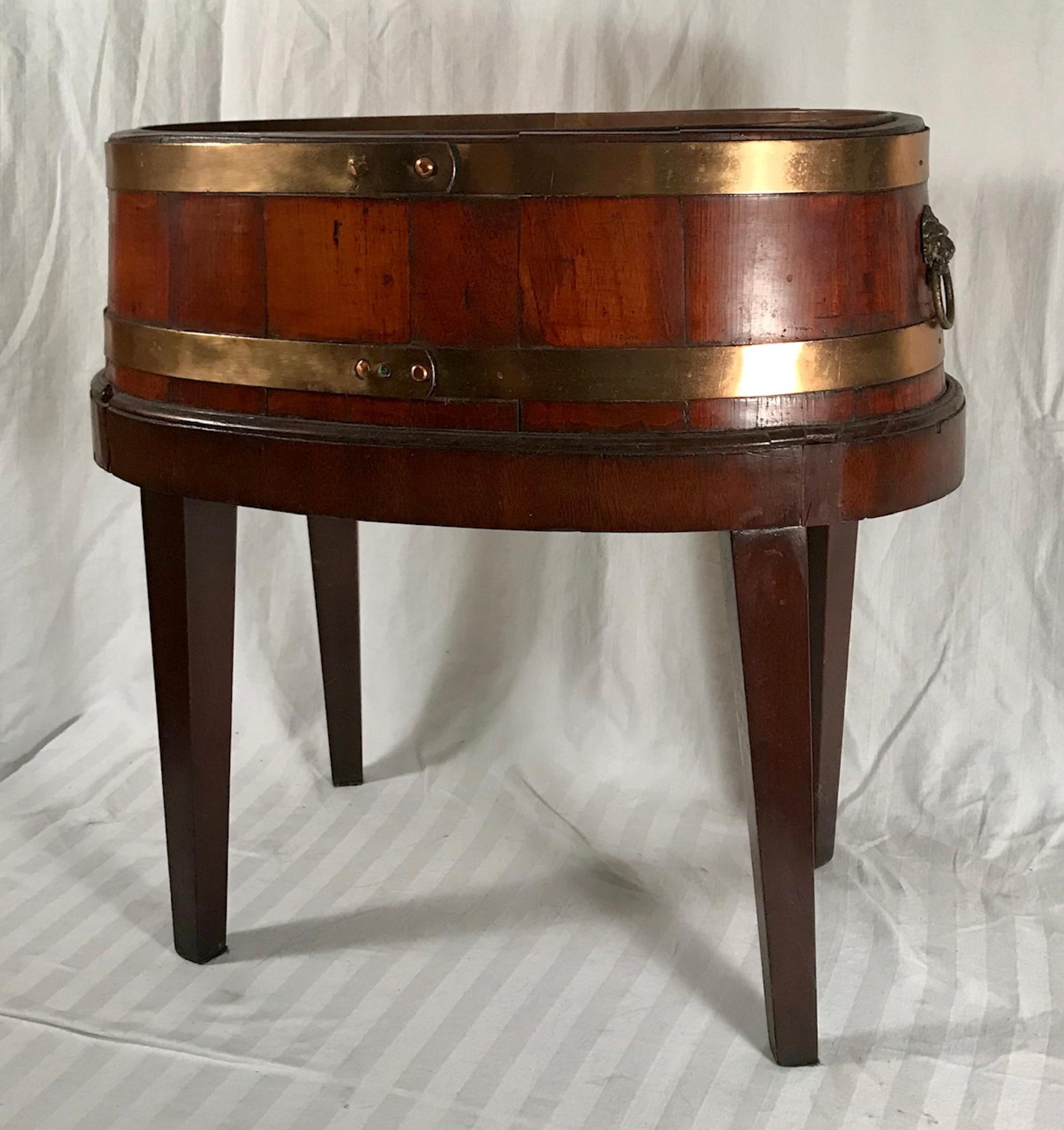 English George III mahogany brass bound cellarette on stand.

A Classic oval mahogany wine cooler with two original solid brass bands. It has an inner removable copper liner. Both ends have mounted brass lion head pulls with rings. The cellarette