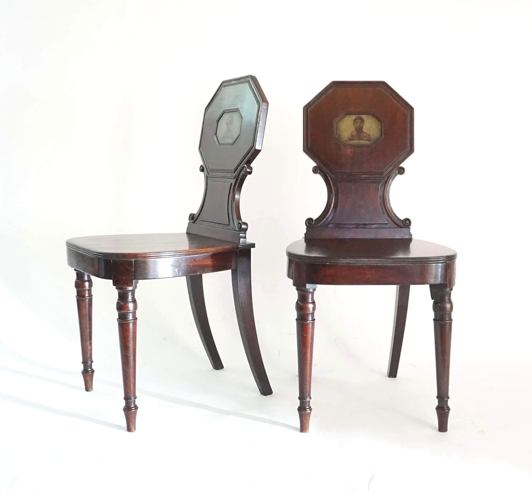 A fine pair of circa 1805 English George III period hall chairs of solid mahogany construction having octagonal tablet form back-rests with original hand-painted Adair family armorial heraldic crest of 'Savage's Head' on side-scrolled plinths