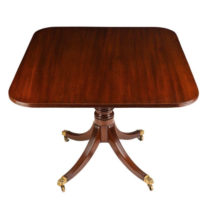 English George III Sheraton mahogany tilt top breakfast table. The table top rests on a square platform with a cast brass latch and is supported by a turned pedestal on four reeded sabre legs which terminate in cast brass lion’s paw feet with