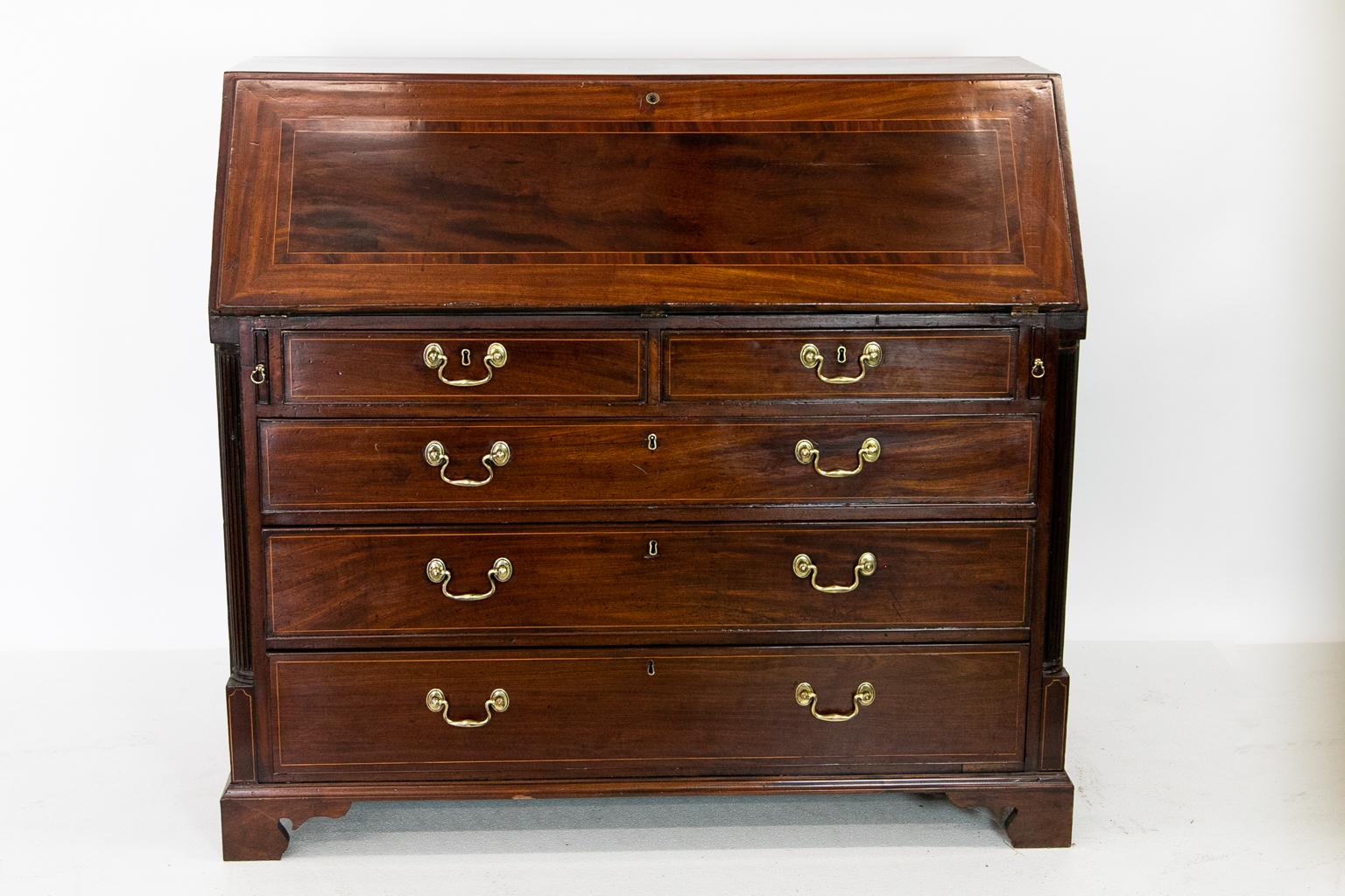 English George III slant front desk is inlaid with boxwood line and crossbanded in mahogany. The interior has inlaid pilasters with secret compartments. There are multiple arched cubby holes.
