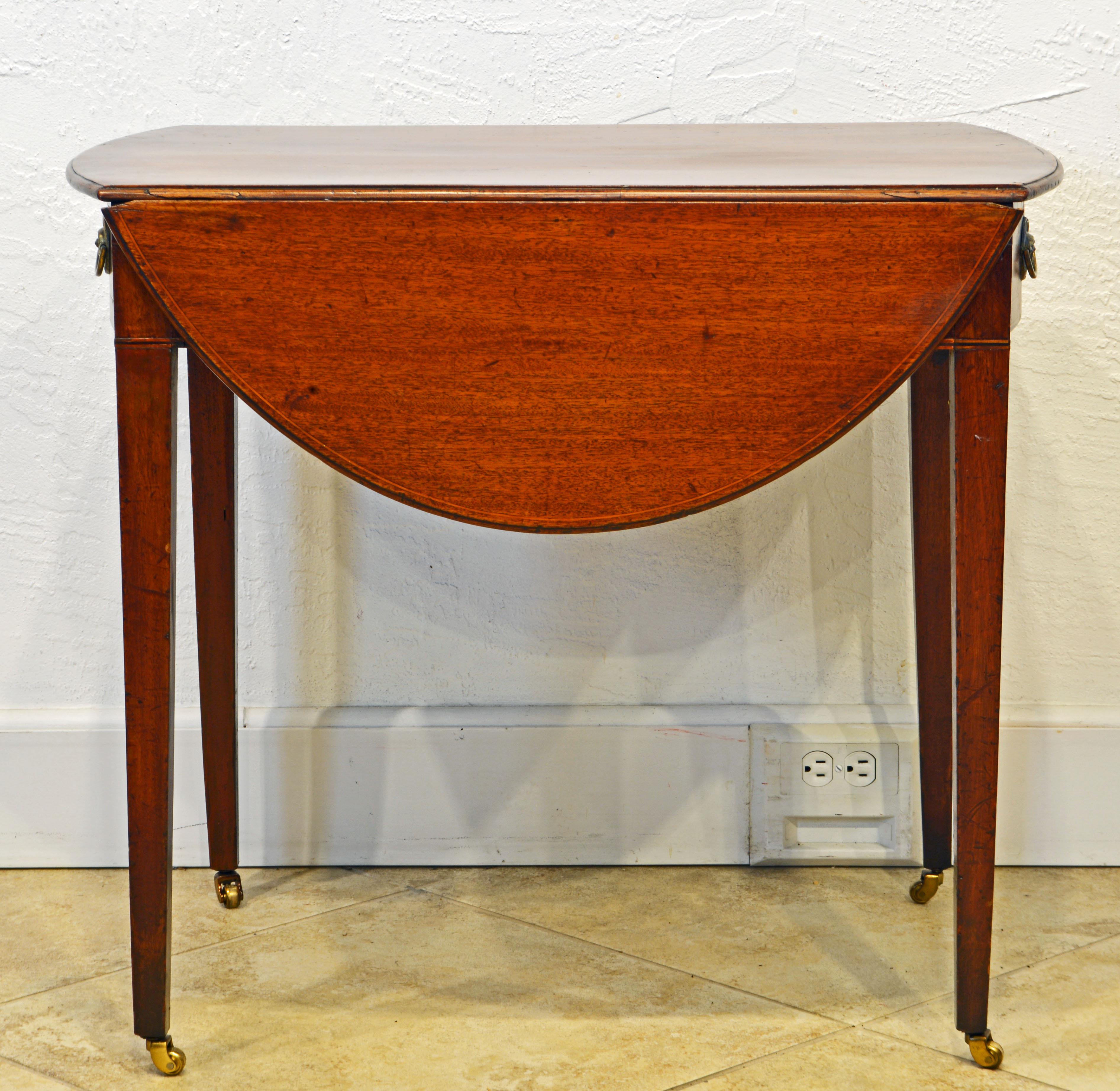 This Classic English George III string inlaid mahogany Pembroke table has two drop leaves that fold up making a larger oval table. The bow front end contains a frieze drawer the other end a simulated drawer. The elegant square tapering legs end in