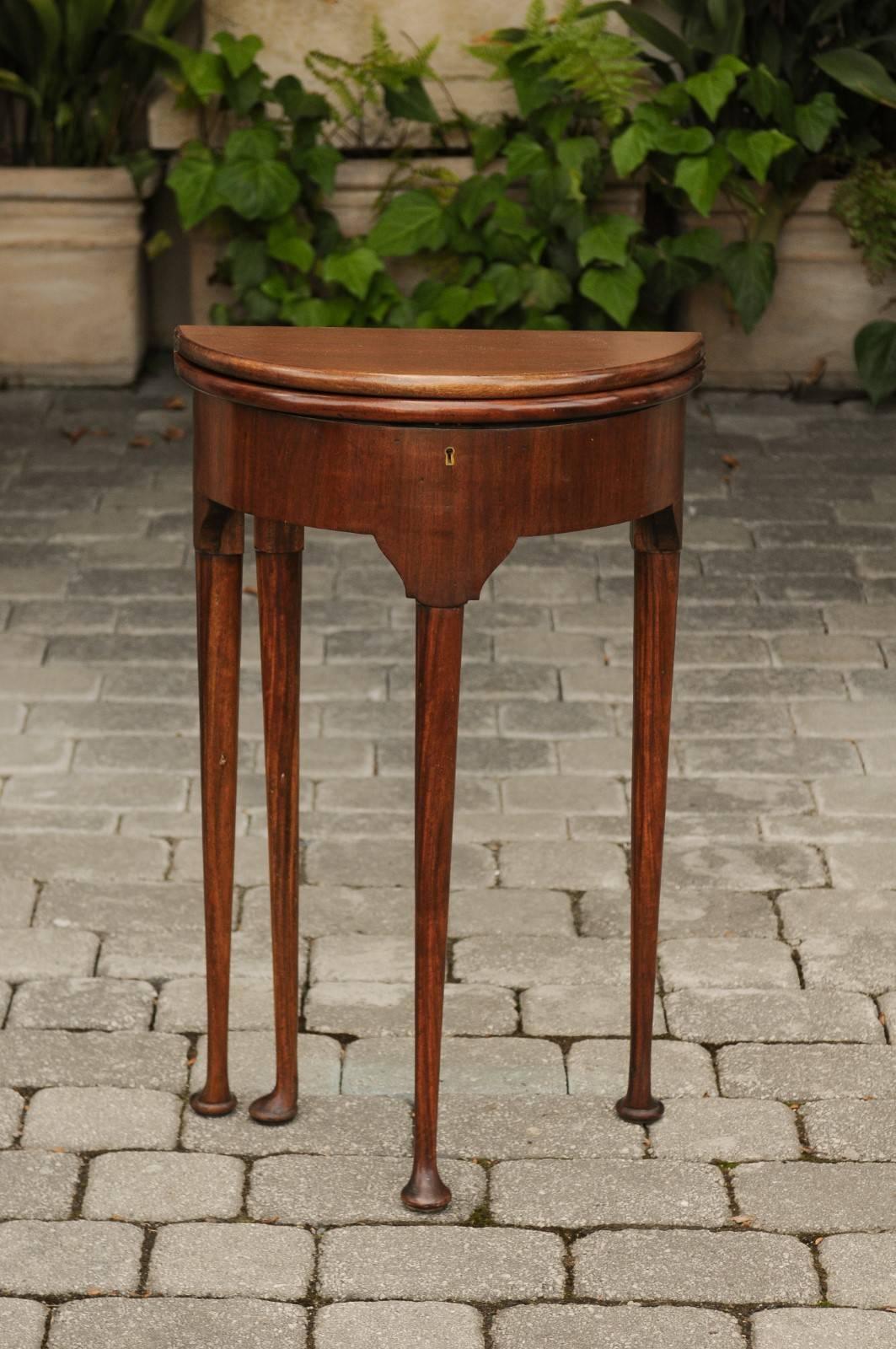 An English George III style petite mahogany demilune table from the mid-19th century, with lift top, storage area and pad feet. This English mahogany demilune table features a semi-circular top with rounded edges, that opens to double as a round