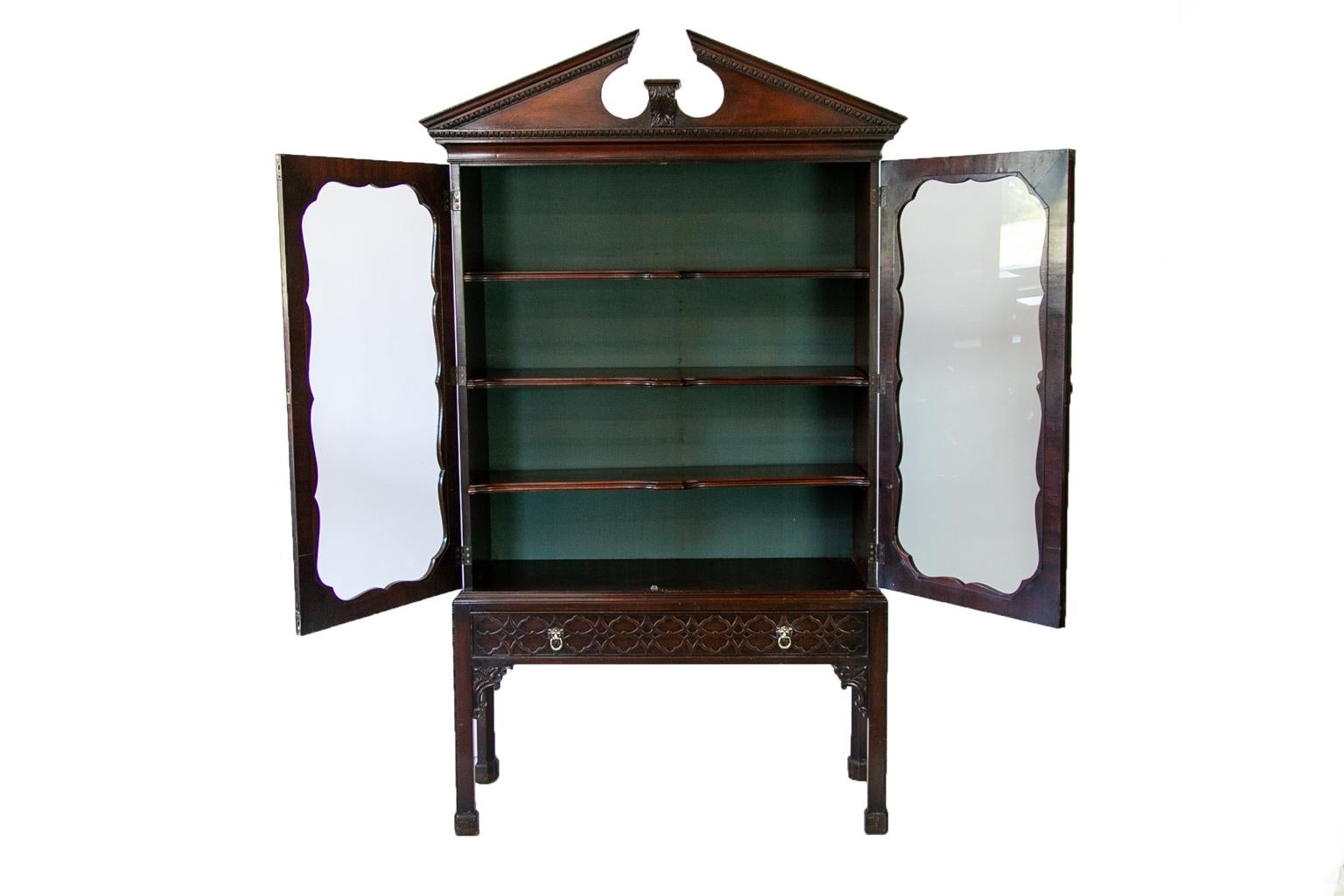 English George III Style Book/Display Cabinet has the original broken arch cornice that has carved egg and dart molding. The doors have cross banded, molded, and scalloped framing. There are carved floral corners. The lower section has one drawer