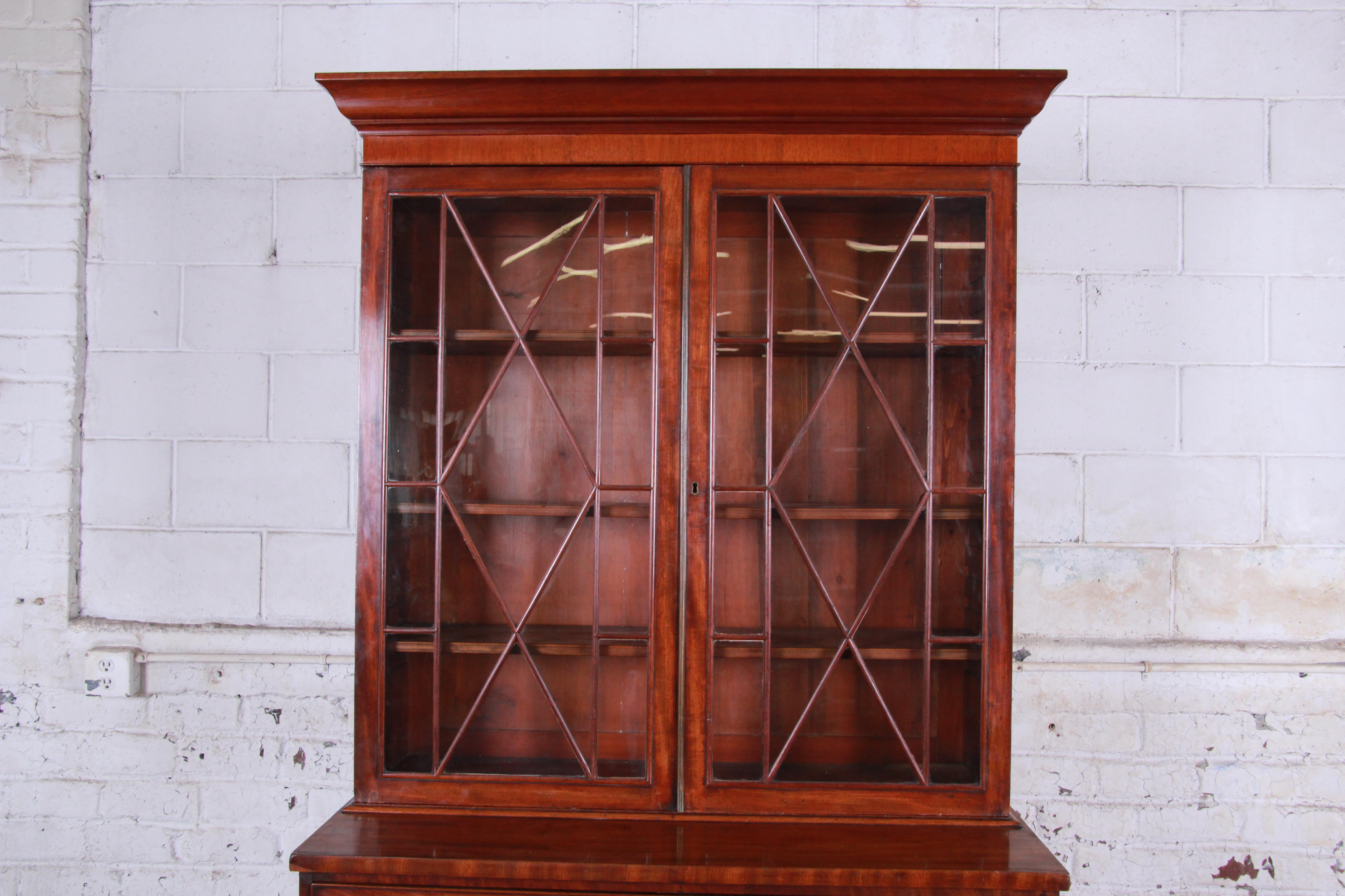 A gorgeous 19th century English George III style secretary desk with bookcase. The desk features beautiful mahogany wood grain, with cherrywood door fronts. It offers ample storage, with a glass front bookcase top with three adjustable shelves, a