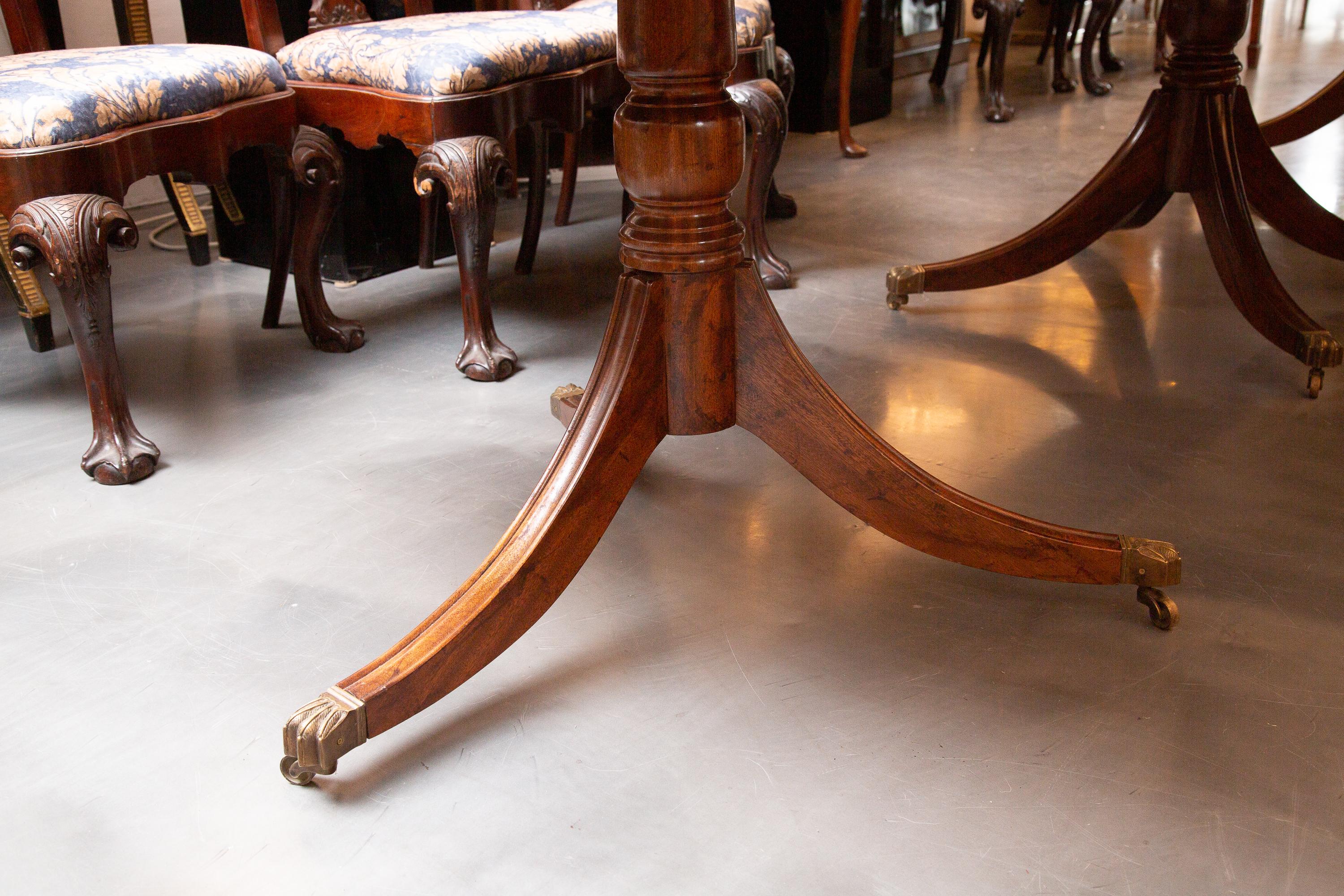 This is a very mellow classic George III style mahogany dining table. The top with reeded edge is supported by three baluster pedestals on scrolling legs terminating in brass casters, 19th century.