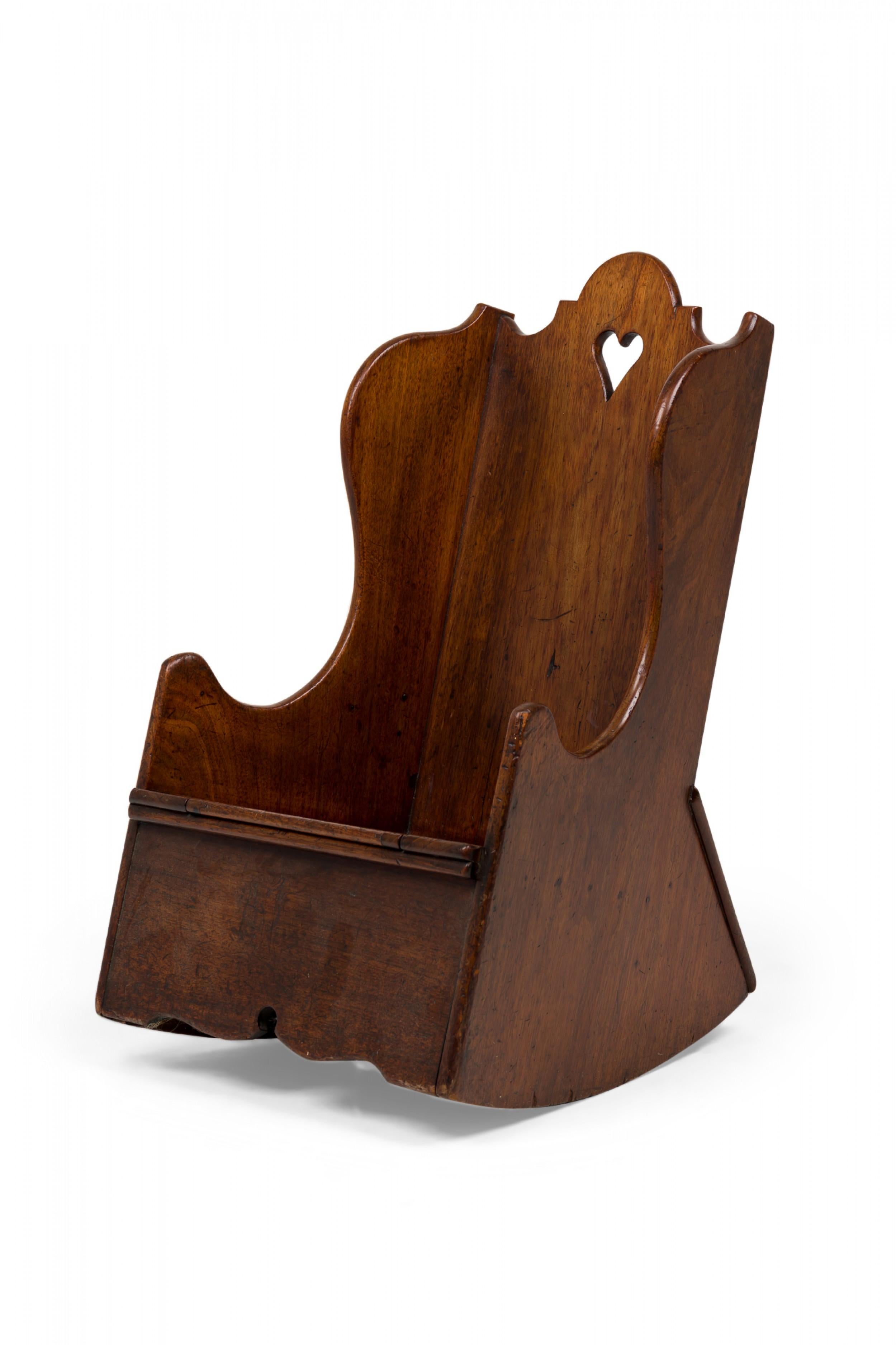 English George III wooden child's rocking chair with wing arms and shaped top rail above a cut-out heart shaped handle slot, the seat composed of 3 segments, the center of which opens as a hinged lid to reveal a circular opening.

Condition: Good;