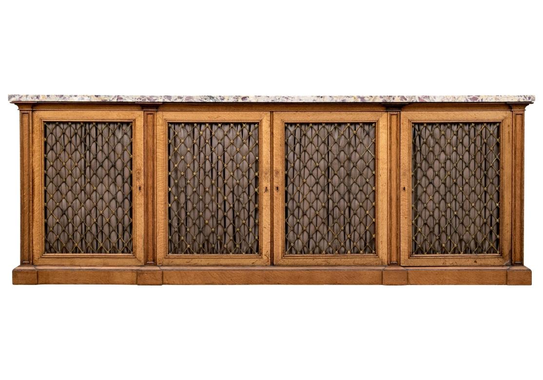 An extraordinary antique English George IV library cabinet circa 1820. Features a long, rectangular breche marble top in beautiful white, orange, and violet, surmounting a stately body of four cabinet doors with gilt brass grills detailed by