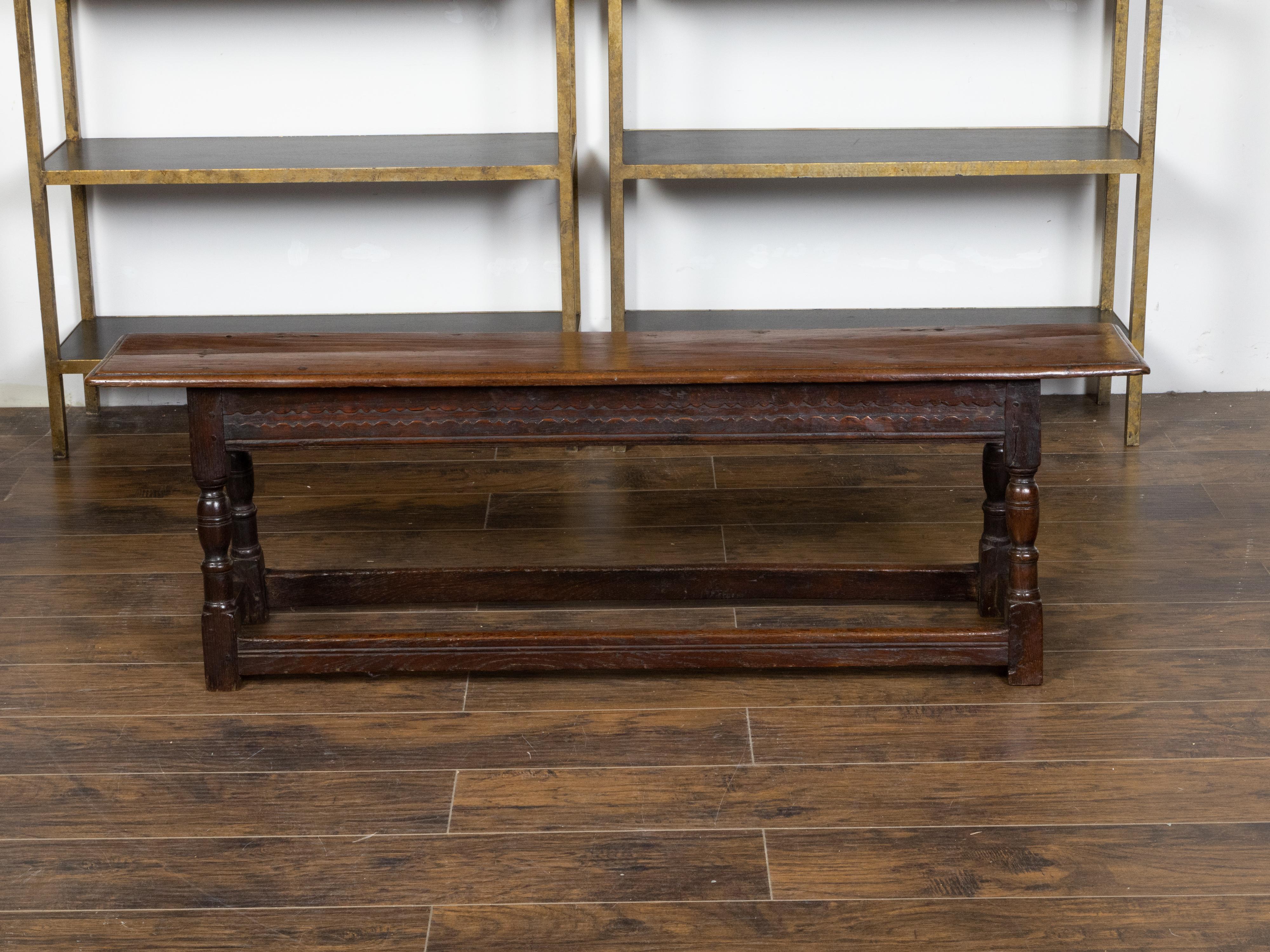 An English Georgian period oak bench from the early 19th century, with simply carved apron, turned splaying baluster legs and plain side stretchers. Created in England during the early years of the 19th century during the late Georgian era, this oak