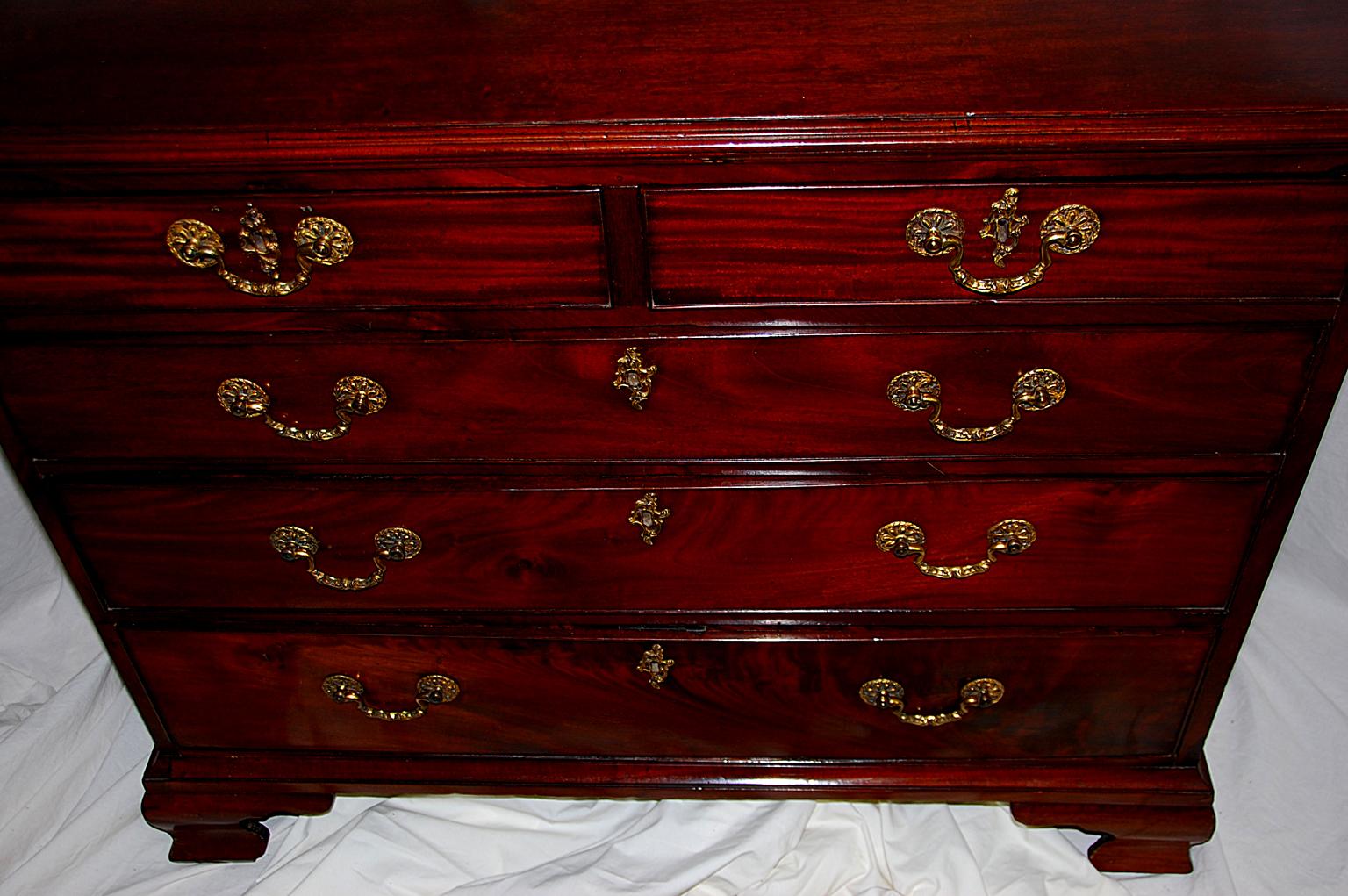 English George III mahogany Chippendale chest of five drawers (two over three) with ogee bracket base and original brass parcel gilt handles and escutcheons. This handsome chest has a slight bow to the drawer fronts; the drawer linings are in oak,