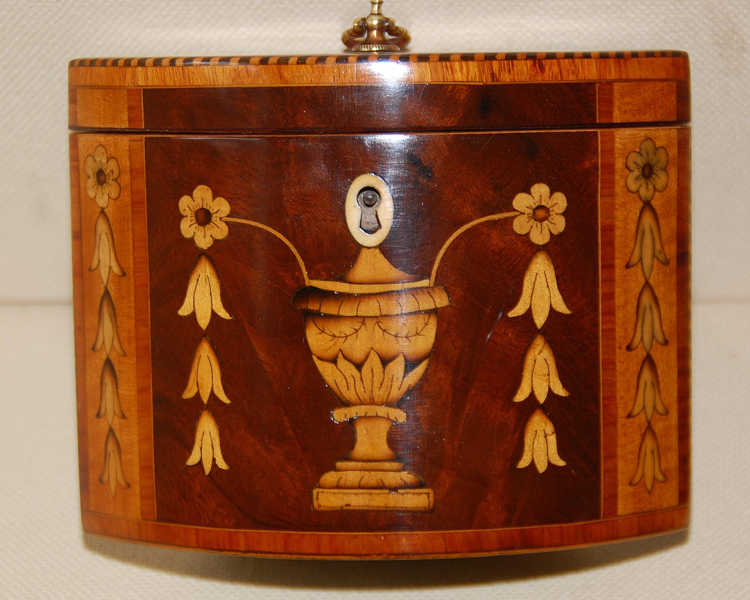 English Georgian 18th century oval tea caddy with urn, flower and husk inlays. This unusual oval caddy has acute angles at both ends which frame the inlays of the front. The mahogany top has fan inlay in boxwood with tulipwood crossbanding and rope