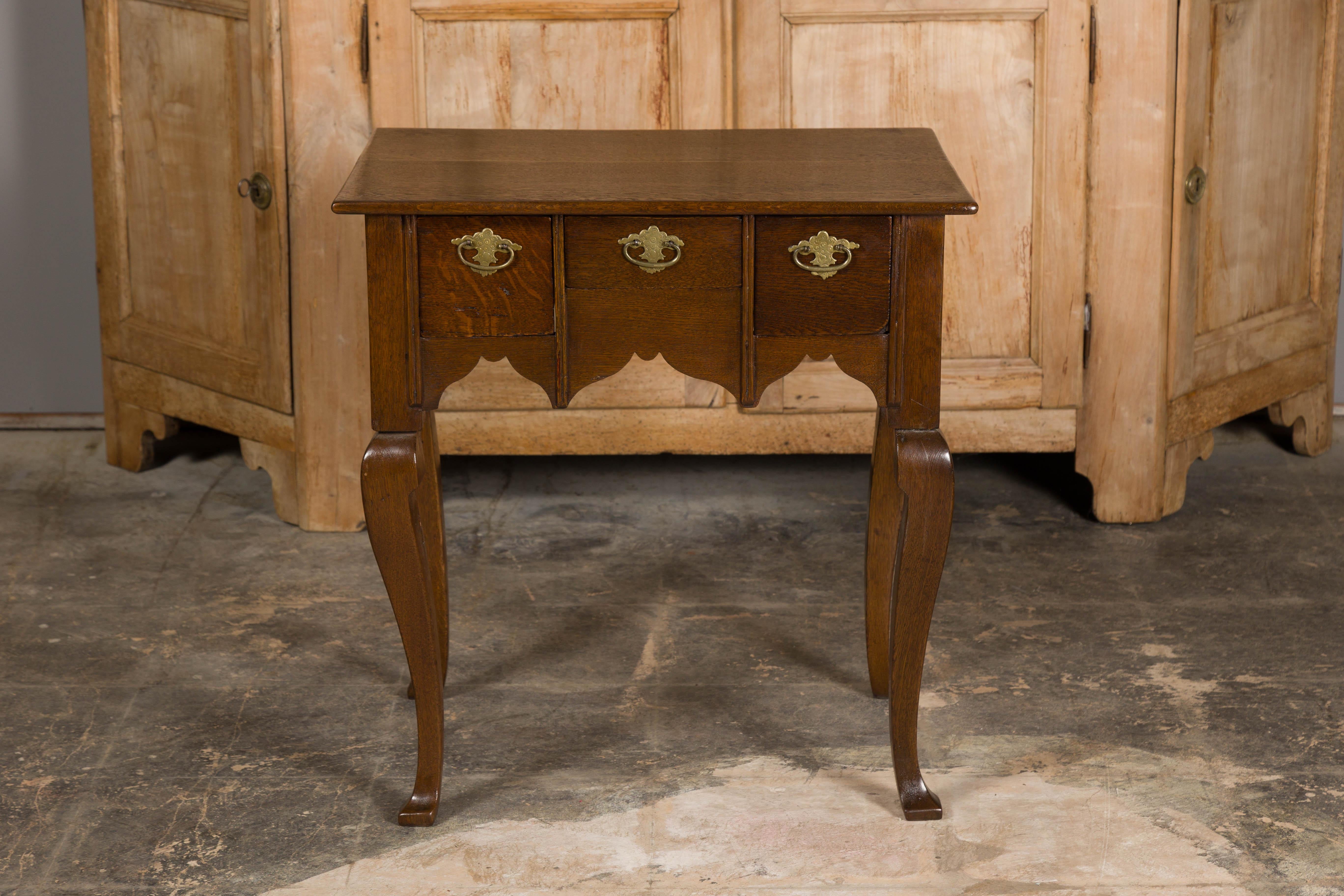 An English Georgian oak table from the 19th century with three drawers and cabriole legs. This English Georgian oak table from the 19th century is a testament to enduring craftsmanship and timeless design. With its classic features and versatile