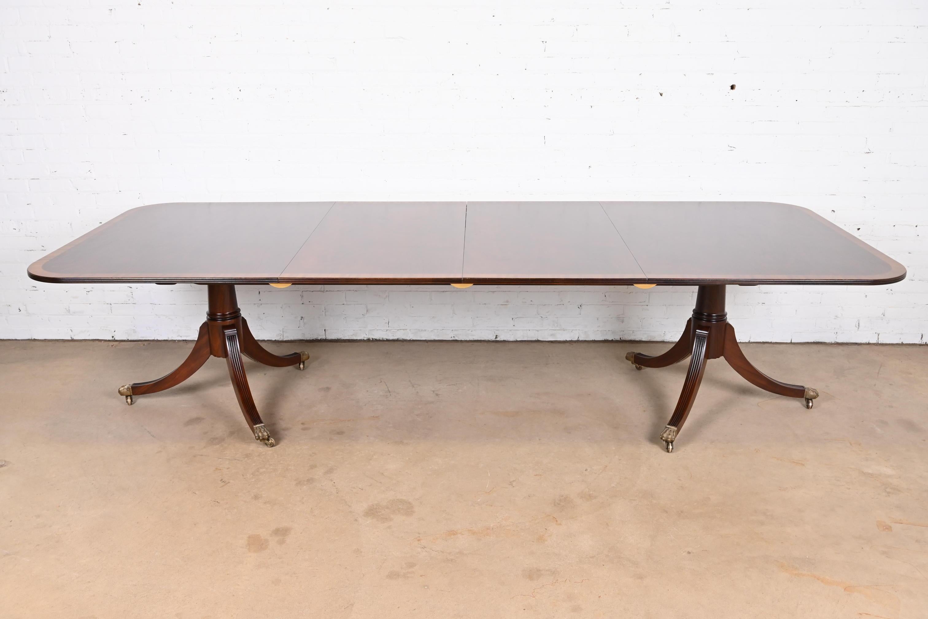 An exceptional Georgian or Regency style double pedestal extension dining table

In the manner of Baker Furniture

England, Circa 1980s

Beautiful mahogany top, with satinwood banding, carved solid mahogany pedestals, and brass paw feet on brass