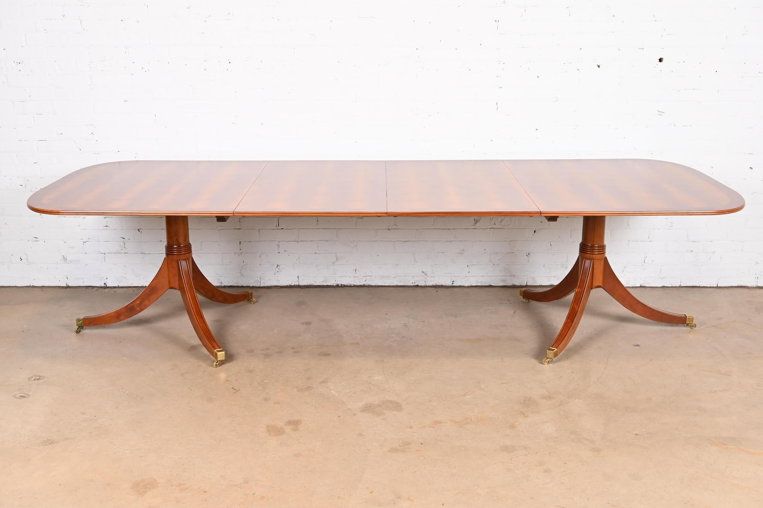 An exceptional Georgian or Regency style double pedestal extension dining table

In the manner of Baker Furniture

England, Mid-20th century

Gorgeous book-matched and banded Yew wood top, with carved pedestals and brass-capped feet and