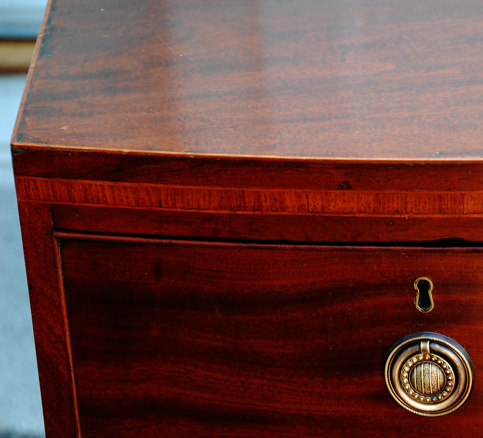 English Georgian bowfront chest of drawers in mahogany with boxwood stringing and harewood crossbanding, French feet and shaped skirt. This small chest is quite versatile being only 35