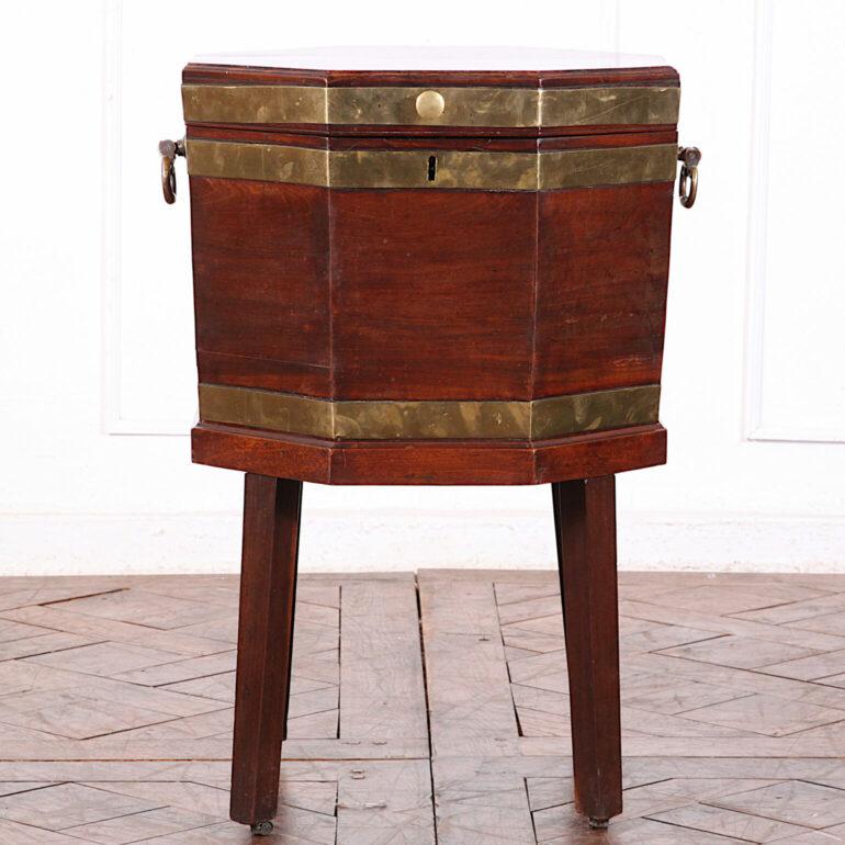 An English Georgian brass-bound mahogany octagonal cellarette or wine cooler with sturdy brass handles and standing on square tapering lets with castors. C. 1800.

 