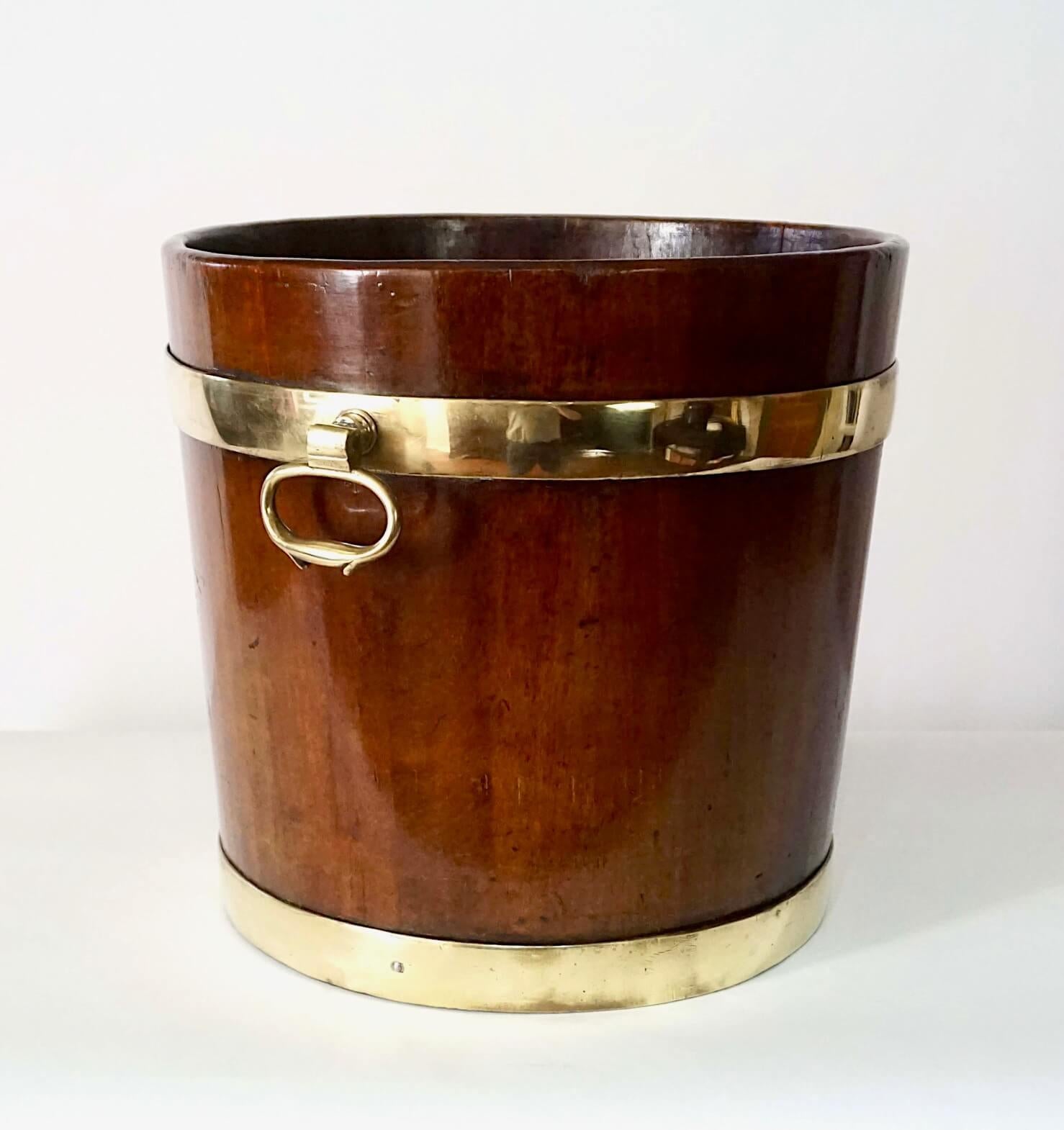 A fine circa 1760 English coal or kindling bucket of brass-bound solid mahogany round tapered stave construction with upper opposing 'Dutch-drop' side handles.  In addition to use around the hearth, it would also make a very chic waste-paper basket