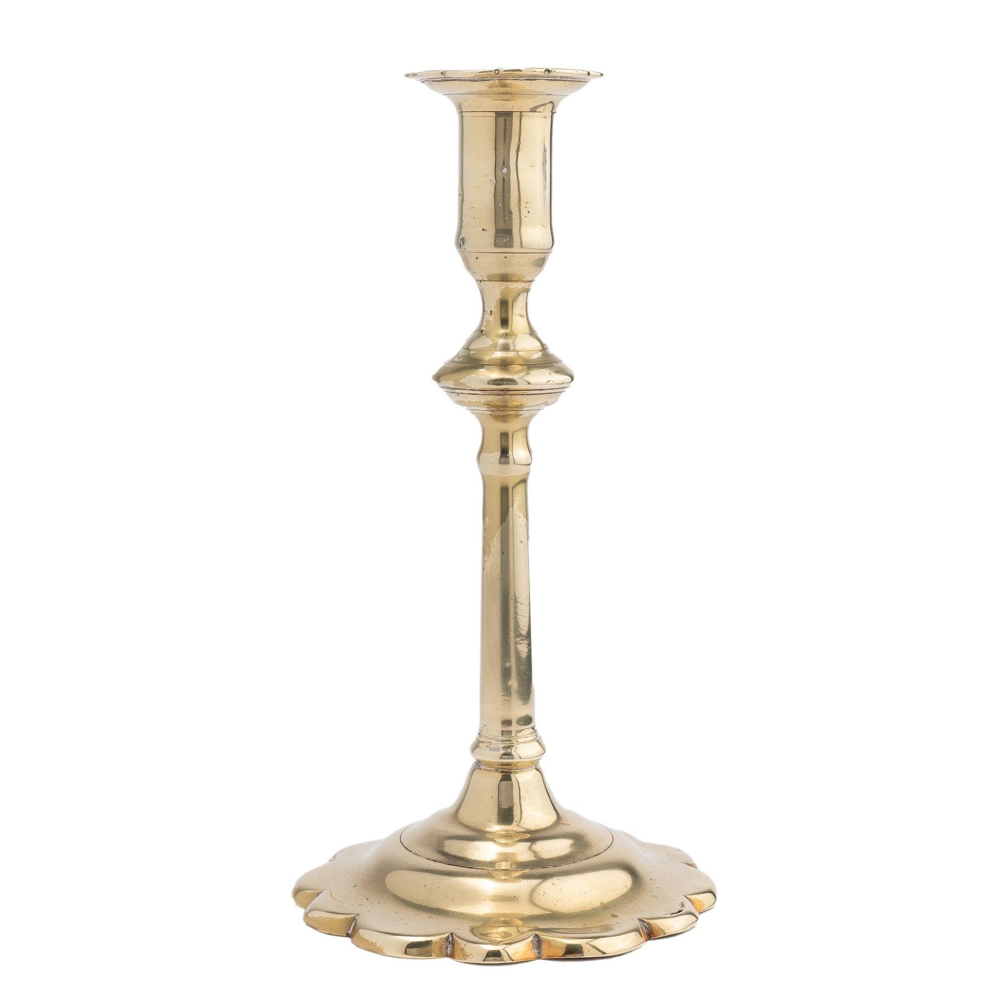 English Georgian cast brass Queen Anne candlestick. The candlestick shaft has a knob directly under the candle cup with a scolloped bobeshe. The candle cup sits above a slightly tapered cylindrical shaft which is peened to a domed base with
