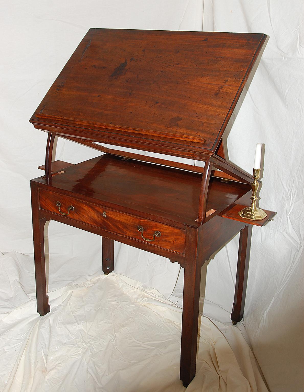 This English Georgian Chippendale period architect's table in mahogany has two side candle slides, a long drawer, and a rising top. The top has a feature that allows it to rise using a double articulating mechanism. There is a removable paper rest