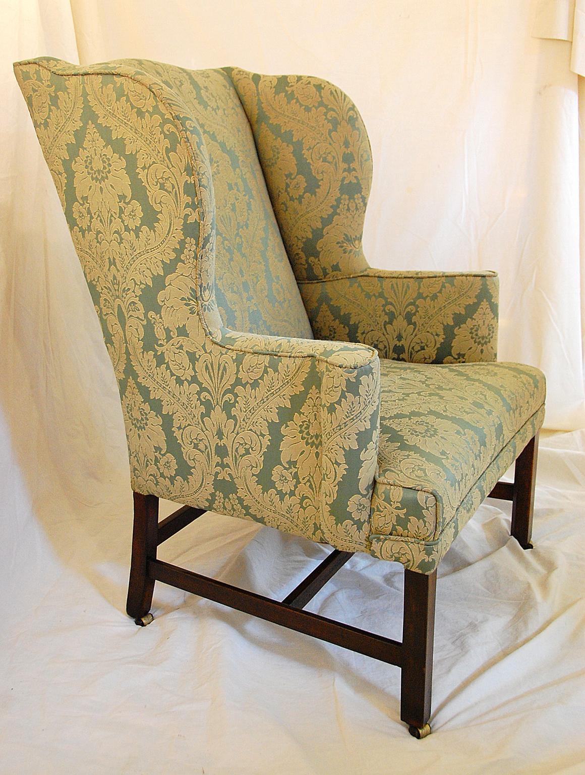 This generous proportioned English Georgian Chippendale mahogany period wing chair with serpentine back rail and graceful side wings leading to scroll out upholstered arms was crafted in the late 18th century. The mahogany square legs are chamfered