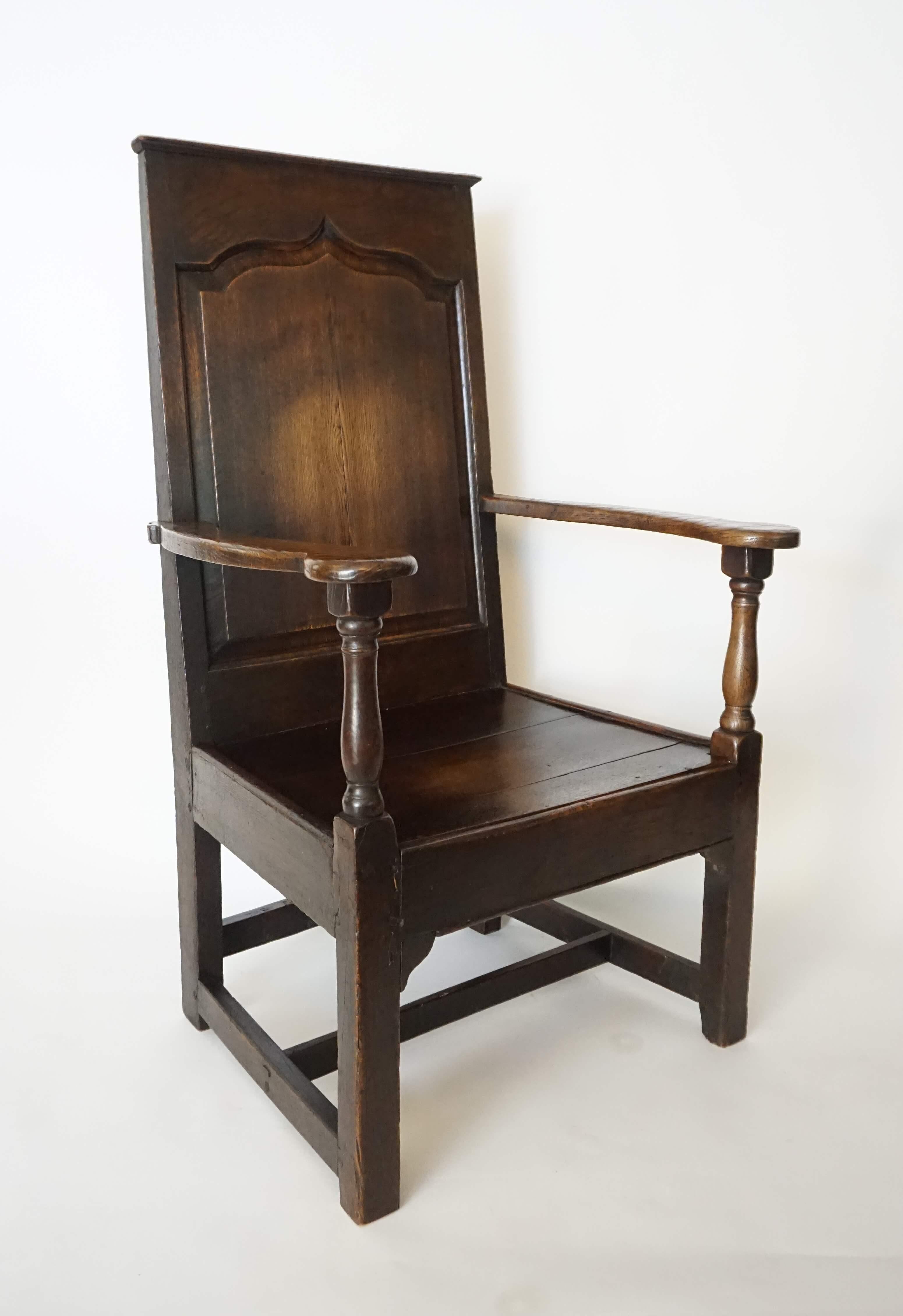English Georgian wainscot armchair having carved elm frame, the 'Gothick' cusped-arch raised-panel rectangular back with molded crest-rail connecting bowed arms on turned balusters and plank seat atop Chippendale influenced bracketed-post form front