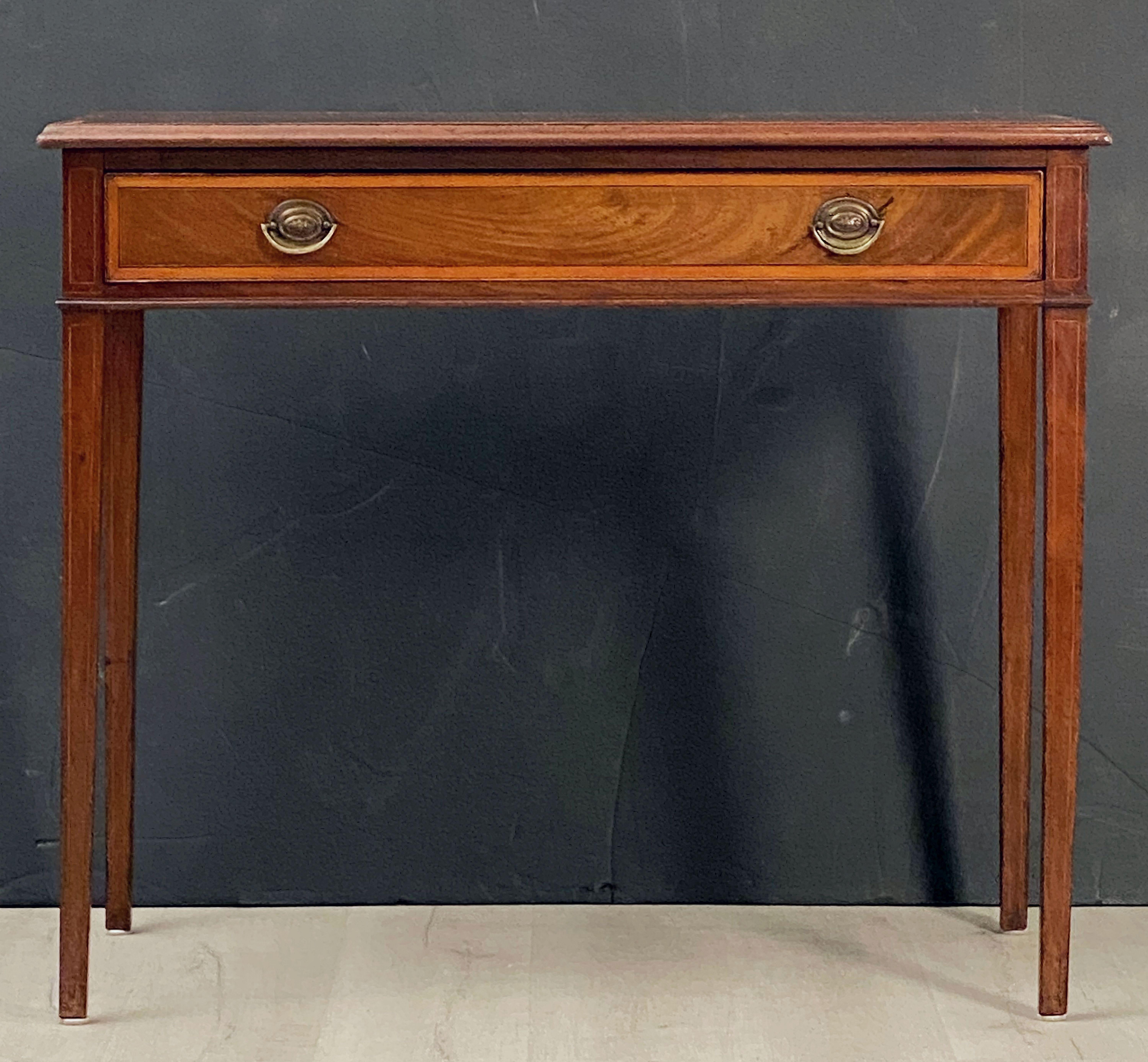 A fine English desk or writing table from the Georgian era, featuring a moulded rectangular top of mahogany with inlaid satinwood edge.
Over a frieze of one long drawer with two brass pulls and displaying lovely flame-cut mahogany veneers with