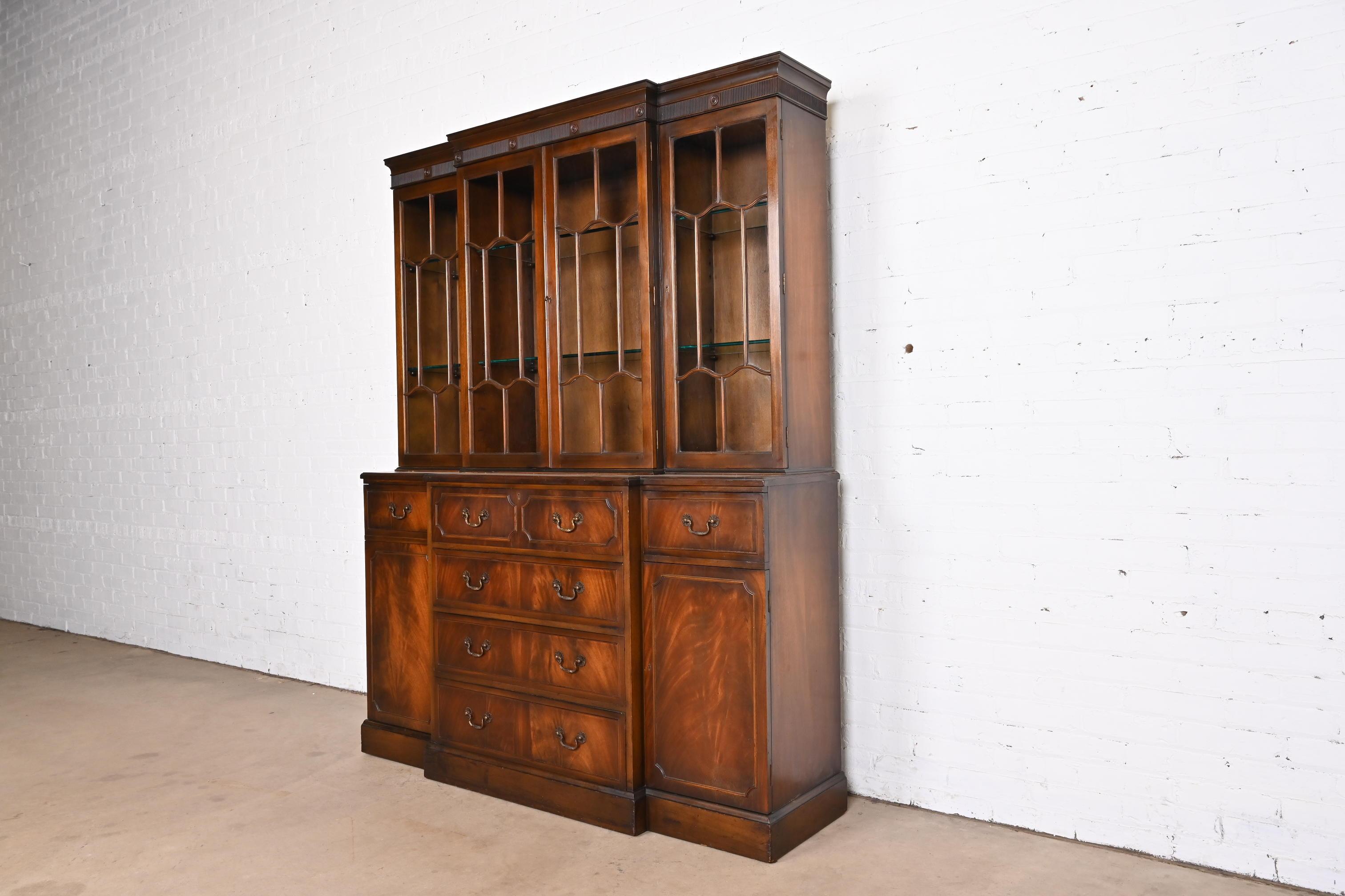 A gorgeous Georgian or Chippendale style breakfront bookcase or dining cabinet

In the manner of Baker Furniture

By Frederick Tibbenham

England, circa 1930s

Carved flame mahogany, with mullioned glass front doors, original brass hardware,