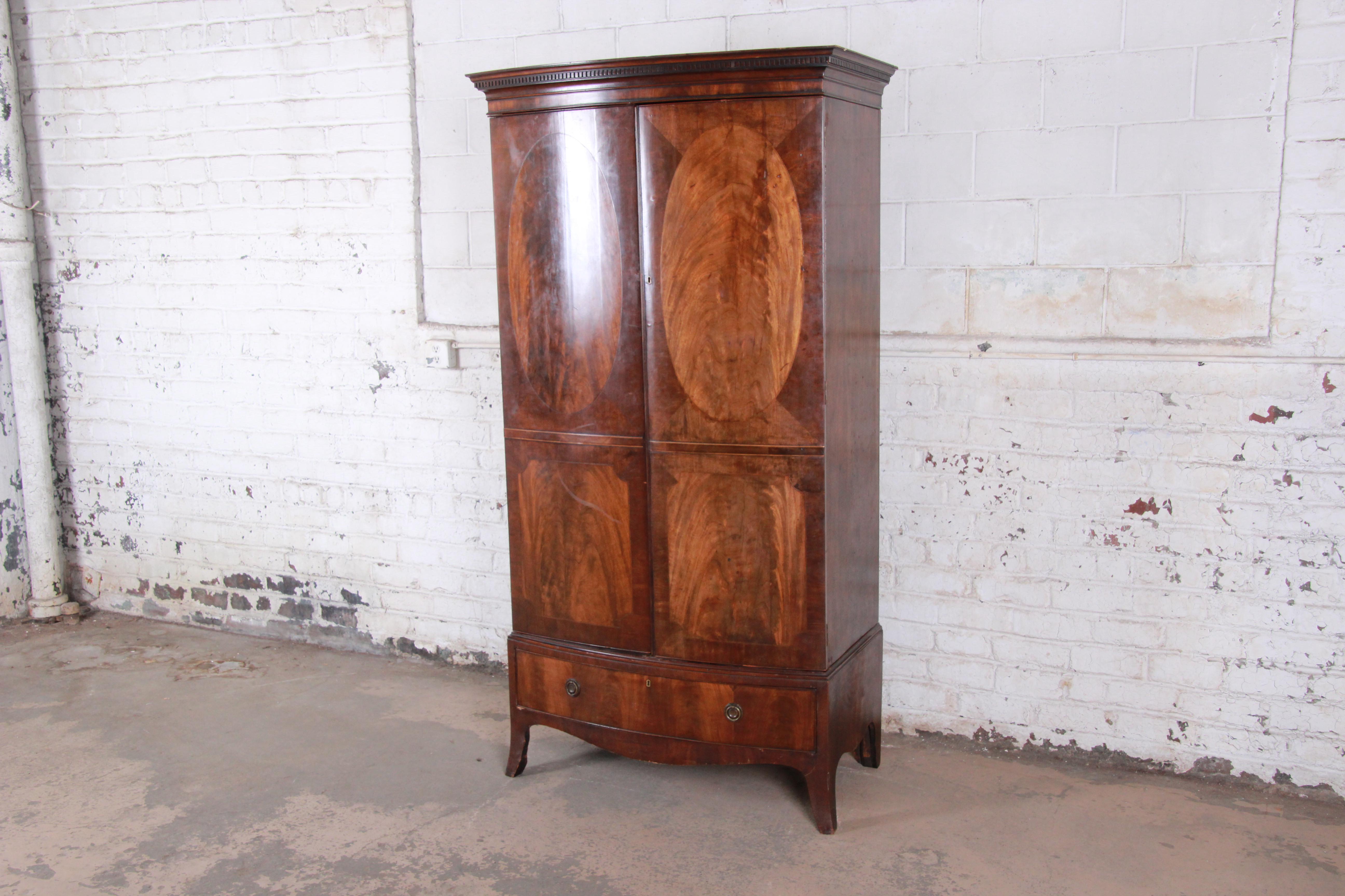 A beautiful antique Georgian linen press or wardrobe. The wardrobe features gorgeous flame mahogany wood grain and nice carved wood details. It offers ample room for storage, with eight cubbies behind two large doors and a single dovetailed drawer