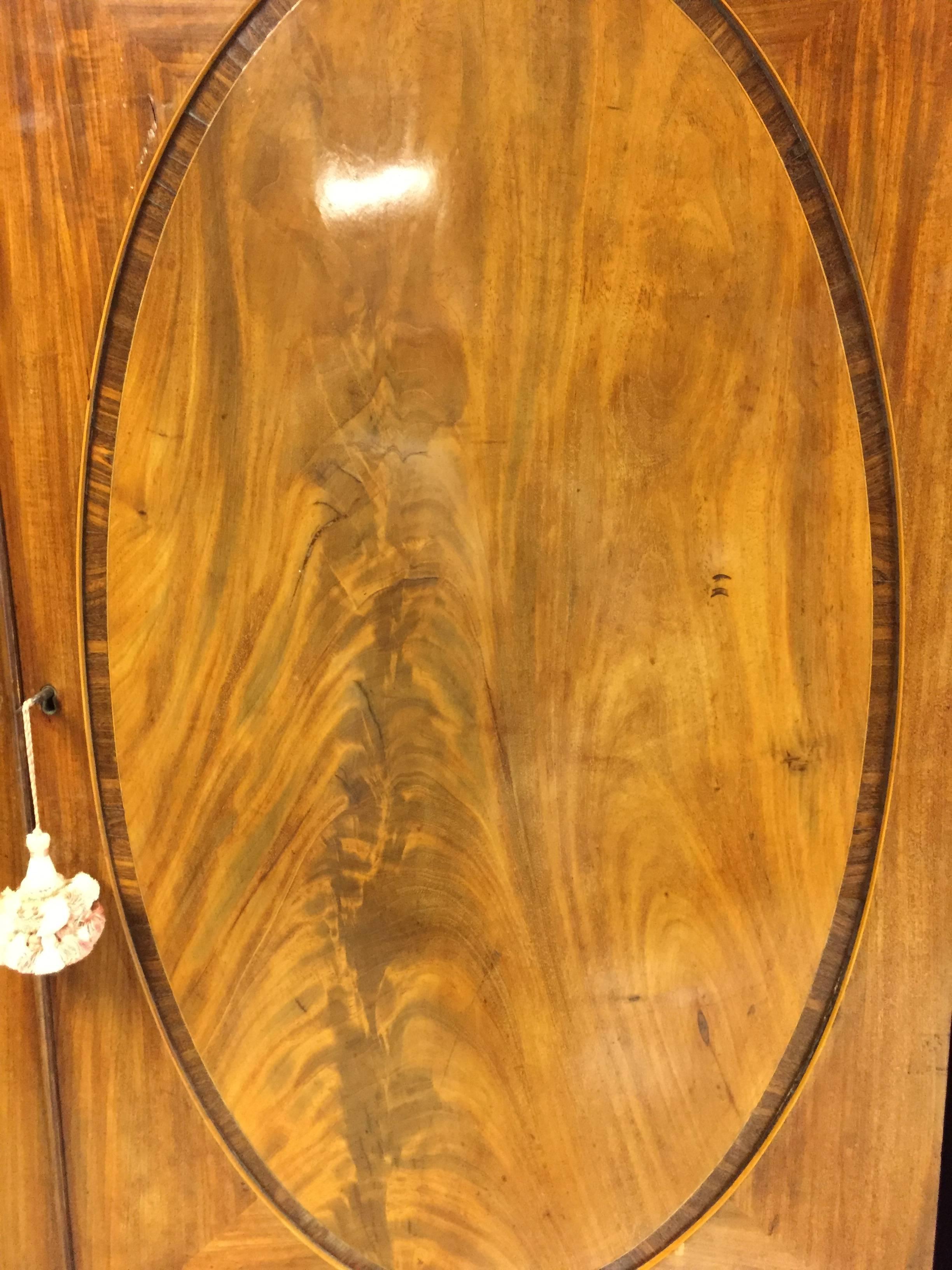English Georgian mahogany linen press with oval panel doors banded with rosewood. C. 1820. Unusual golden walnut color, dentil mold cornice, original bracket feet, Chippendale handle pulls on rosettes, oak interiors, three original slides.