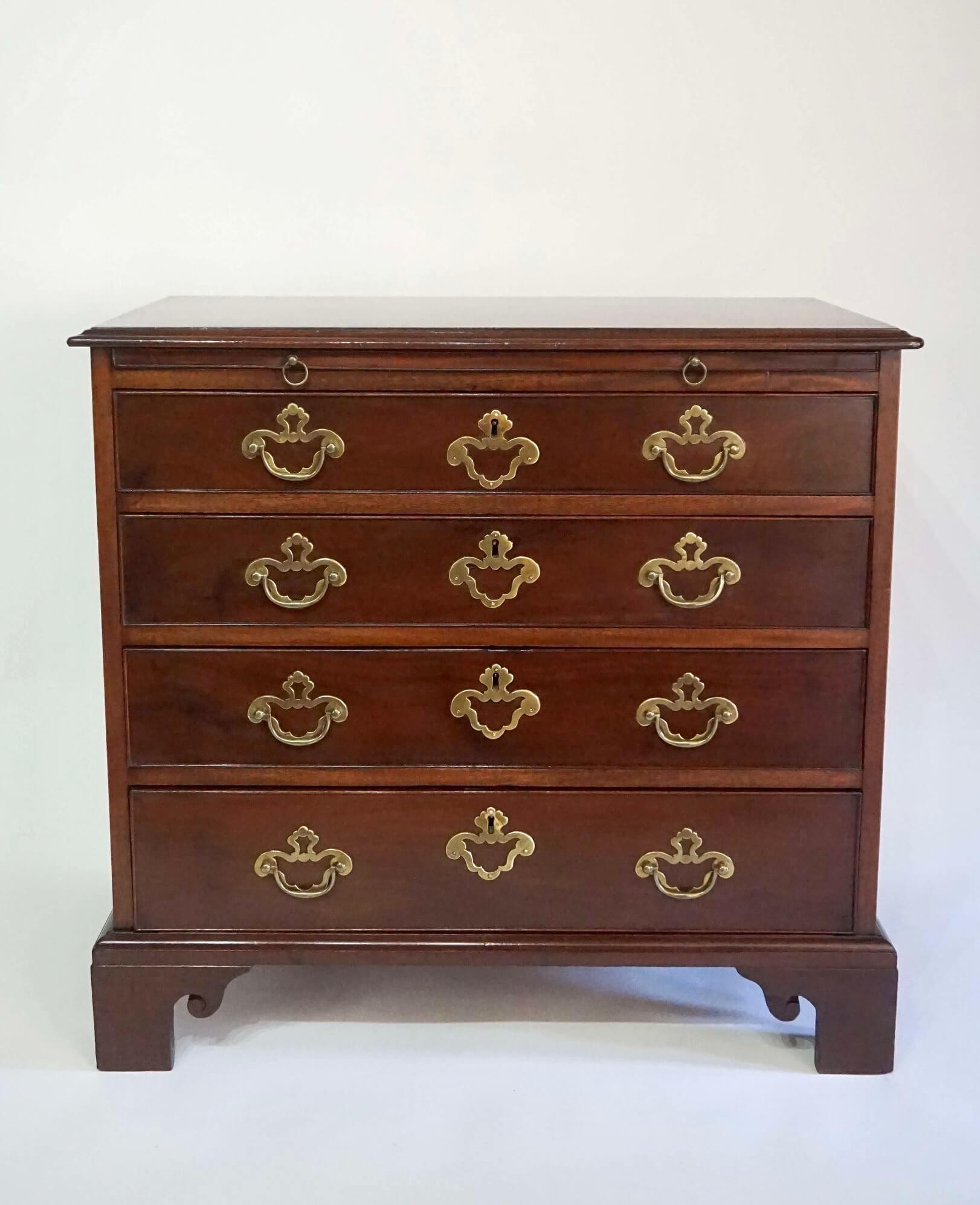 A fine English circa 1760 mahogany bachelor's chest or petite commode having single solid board top with molded edge atop pullout brushing slide over four drawers with original brass hardware on scroll-carved bracket feet.