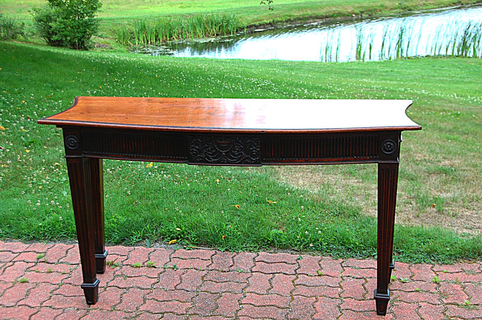 English Georgian period mahogany bowfront sideboard or hall table. The four tapered reeded legs have marlborough feet; the reeding is on three surfaces on the front legs and two surfaces on the back legs so the visual impact is quite strong. The