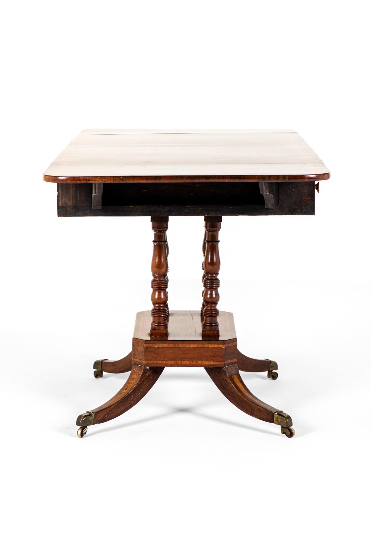 A beautifully presented late Regency period Georgian sofa table in mahogany.

The cross banded double drop leaf top sits above a single frieze drawer with boxwood edge lines flanked by a dummy drawer to either side and four brass handles.

The table