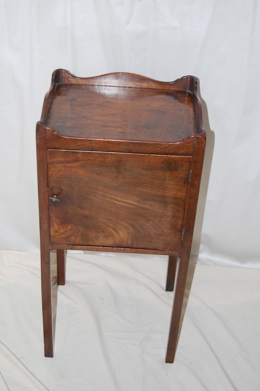 English Georgian mahogany pot cupboard with serpentine galleried top, lambs tongue corners and tapered legs. The cupboard space is accessed from the front of the table via the hinged door. The table is finished on all sides so it can free stand as