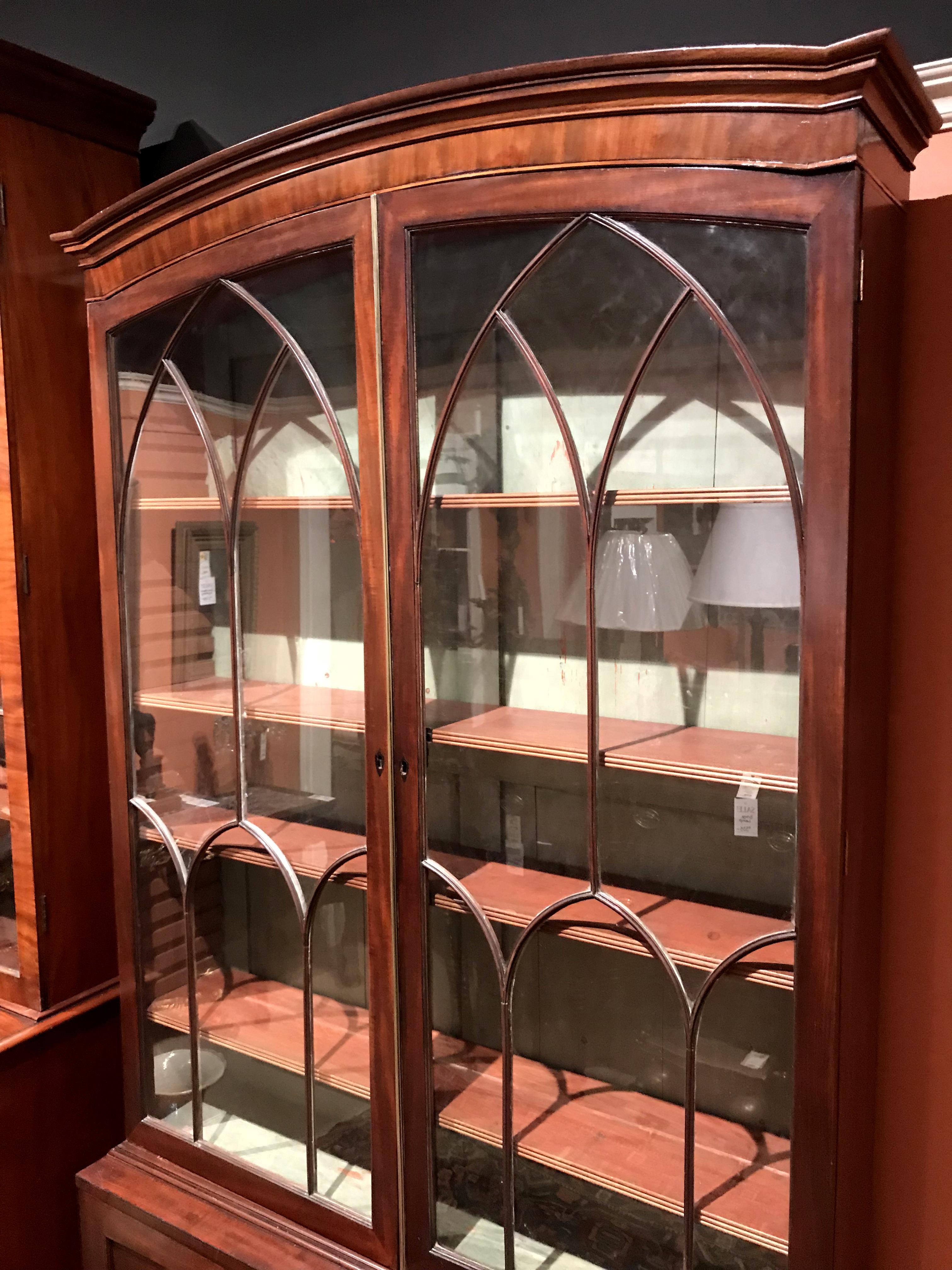 A fine two part English Late Georgian mahogany bookcase or china cabinet with an appealing size and form, its upper case with two Gothic style glazed doors which open to a green painted interior with adjustable shelves, over a lower case with two