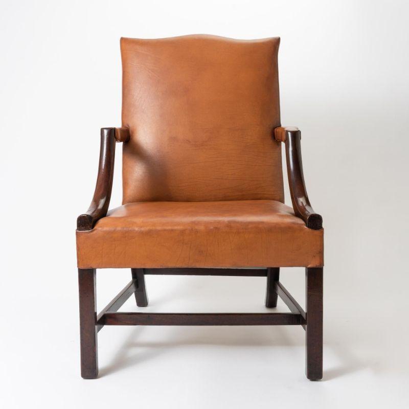 English Georgian mahogany lolling chair upholstered with saddle brown leather. The upholstered back panel has a serpentine crest rail above an upholstered seat. The elbow rests are upholstered and supported by sloping arm brackets. The chair rests