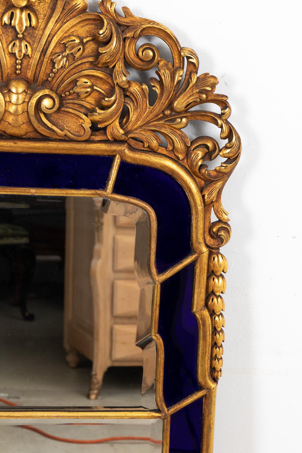 English Georgian style mirror with Venetian blue cobalt glass around the border of the beveled mirror, circa 1890s. The piece also features a detailed giltwood crown with scrolled foliage and a center scallop shell motif. Made in England. Please