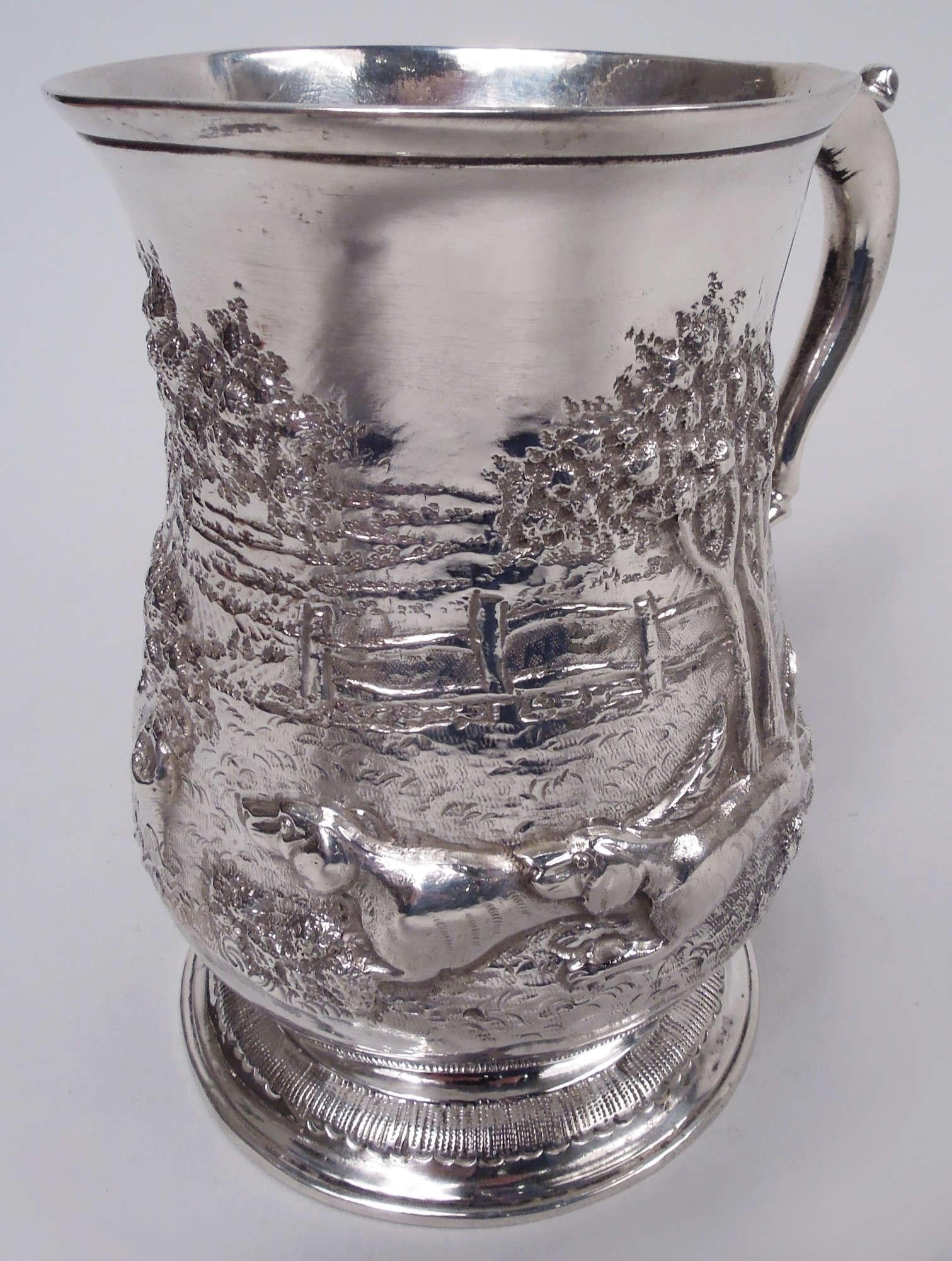 George II sterling silver mug. Made by Samuel Welles in London in 1759. Baluster bowl with leaf-capped double-scroll handle. Raised foot with tooled leaf border. Chased and engraved bucolic scene with hounds racing through an orchard. A later