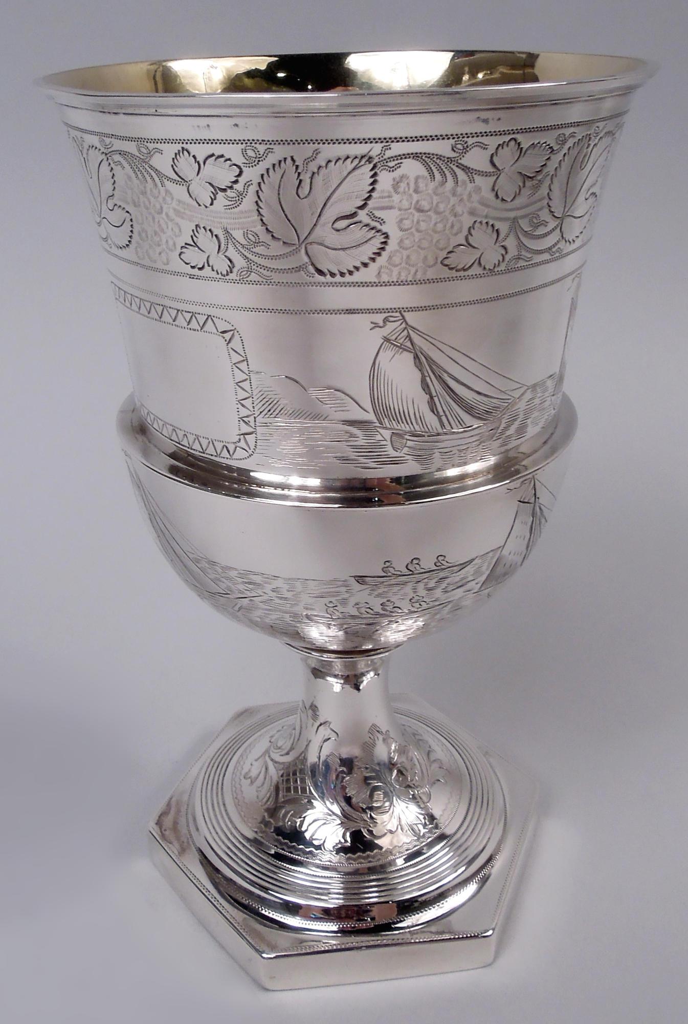 English Georgian Neoclassical sterling silver goblet, 1810. Medici urn bowl; round reeded foot mounted to hexagonal base. Engraved nautical scenes with boats propelled by wind and manpower. Fruiting grapevine band at mouth rim; leafing scroll and