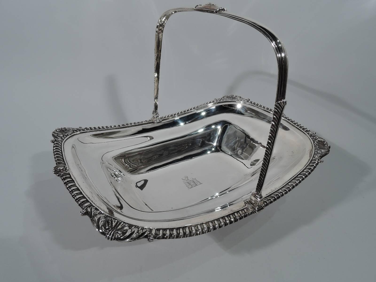 George III sterling silver basket. Made by Thomas Robins in London in 1808. Tapering rectilinear bowl with swing u-form handle and raised foot. Gadrooned rim with shells and leaves. Handle sides leaf-capped. Armorial with lion rampant and turreted