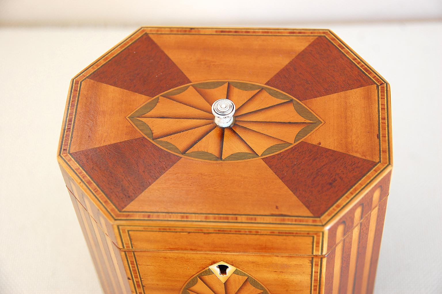 English Georgian octagonal tea caddy in satinwood and mahogany with inlaid columns and fans of stained and shaded boxwood, delicate stringing of crossbanded kingwood, complete with key, bone escutcheon and turned tiny handle to top of lid. The