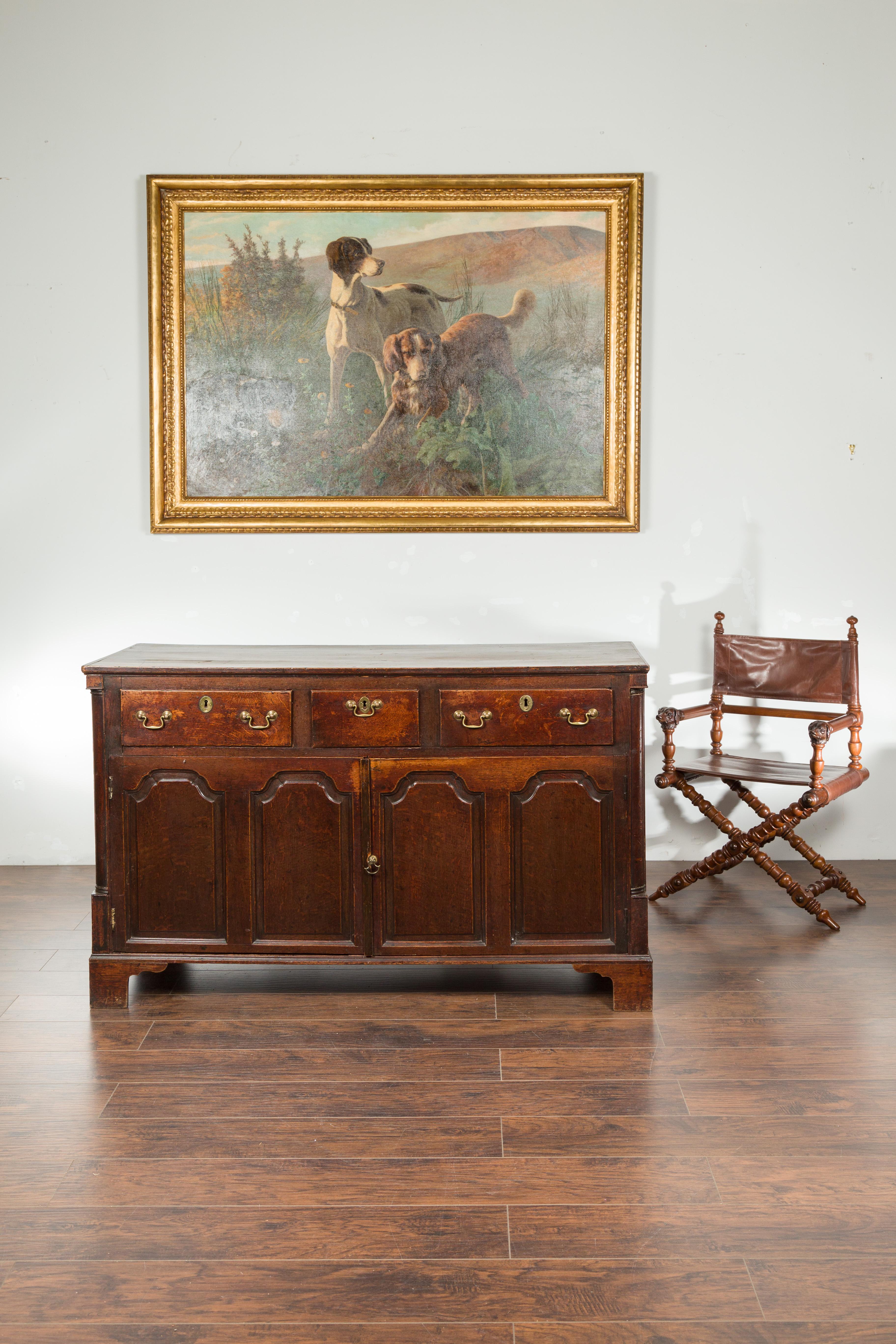 An English Georgian period oak buffet from the early 19th century, with three drawers and two doors. Created in England during the early years of the 19th century, this oak buffet features a nicely distressed rectangular planked top, sitting above